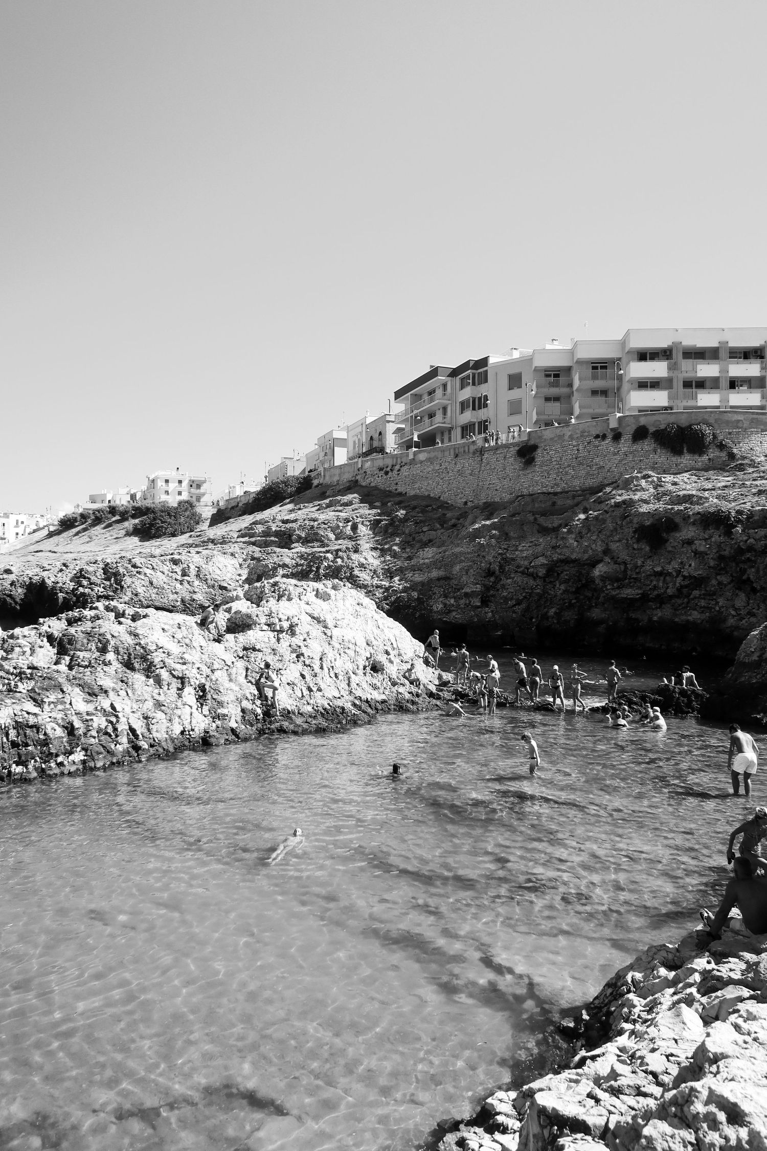 Rocky coastal swimming area with clear waters and limestone cliffs surrounded by modern buildings.