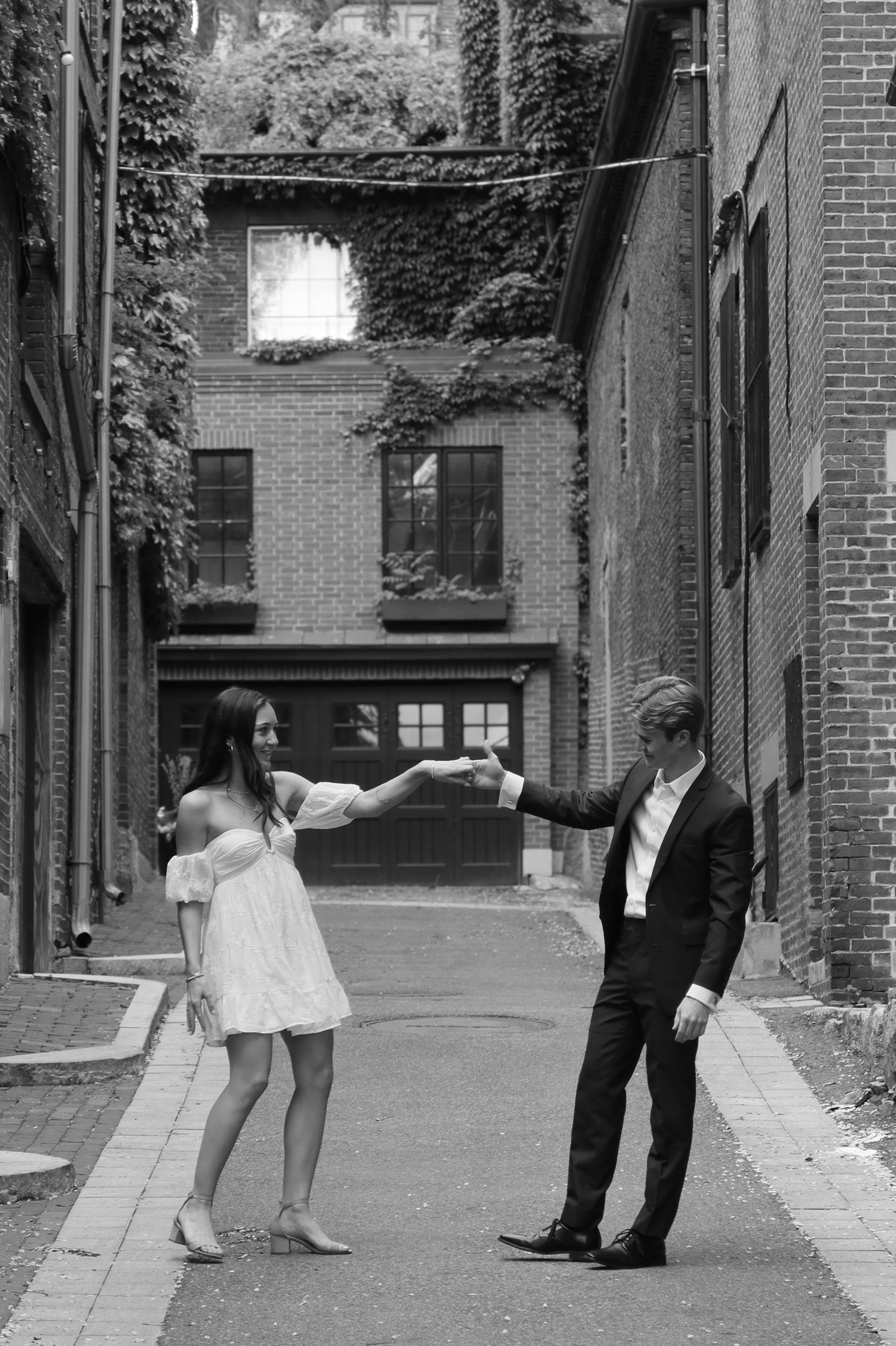 A couple performs dance moves in a sequence of black and white photos on a narrow urban alley.