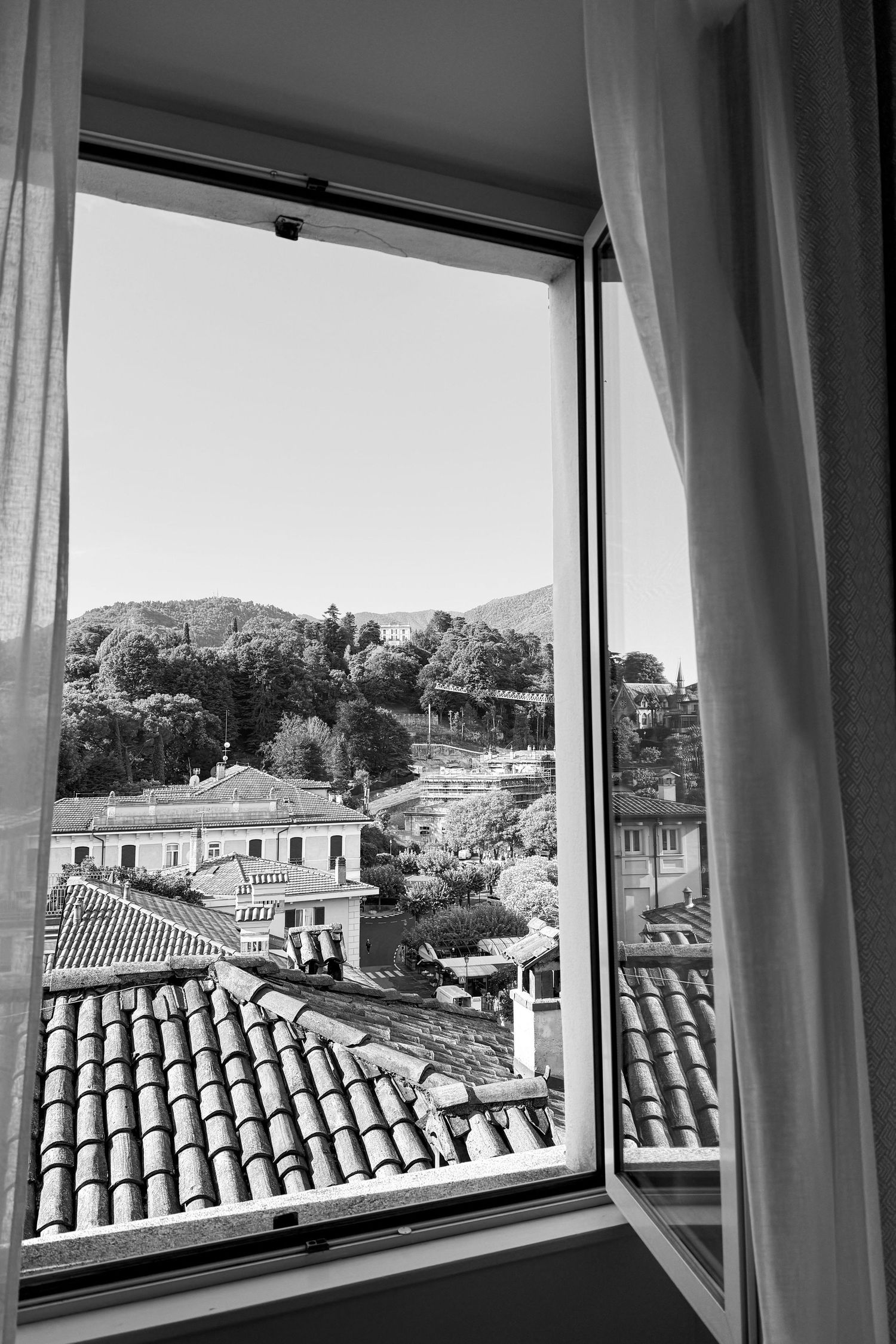 Panoramic view through windows showing Mediterranean rooftops and distant mountains.