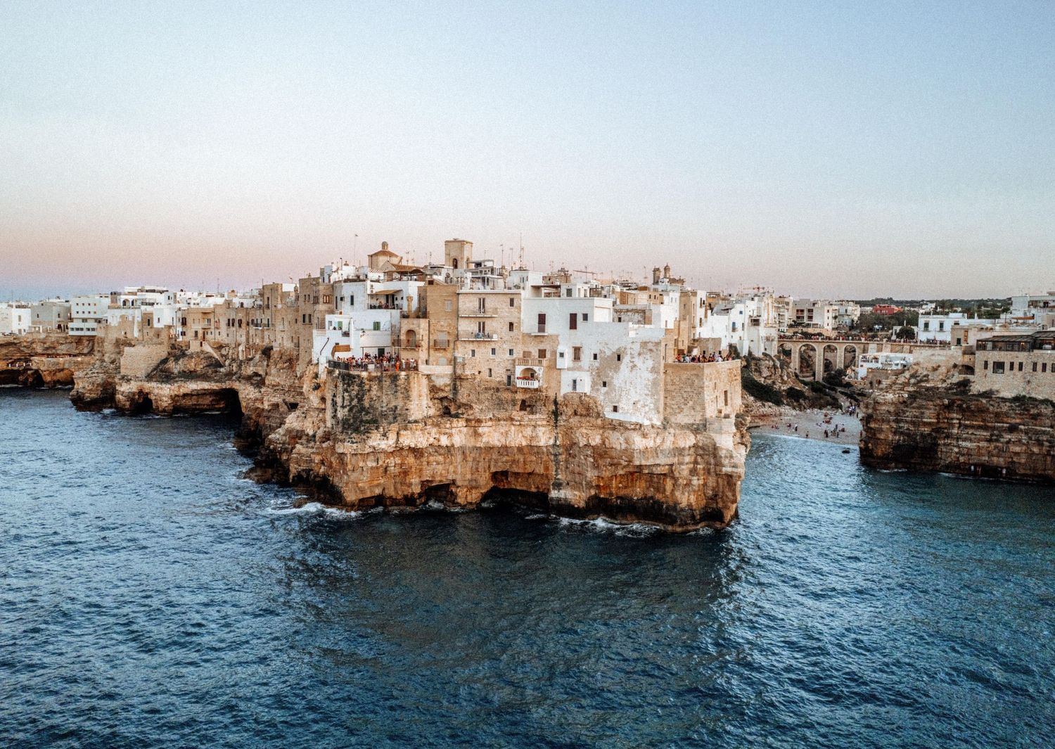 Panoramic view of white coastal buildings perched on limestone cliffs overlooking the Mediterranean Sea at sunset.