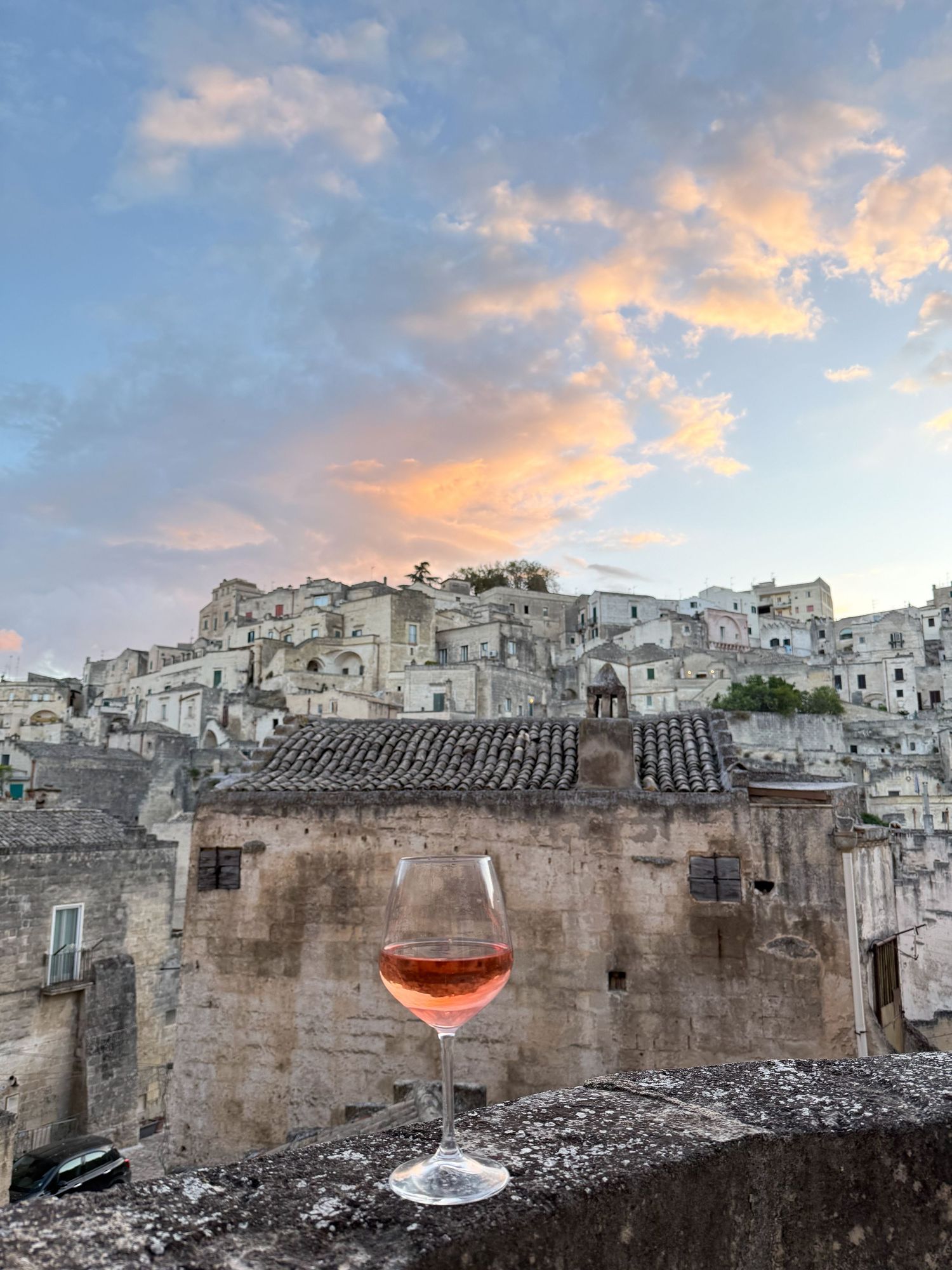 Ancient stone city at sunset with a wine glass silhouetted against the historic architecture.