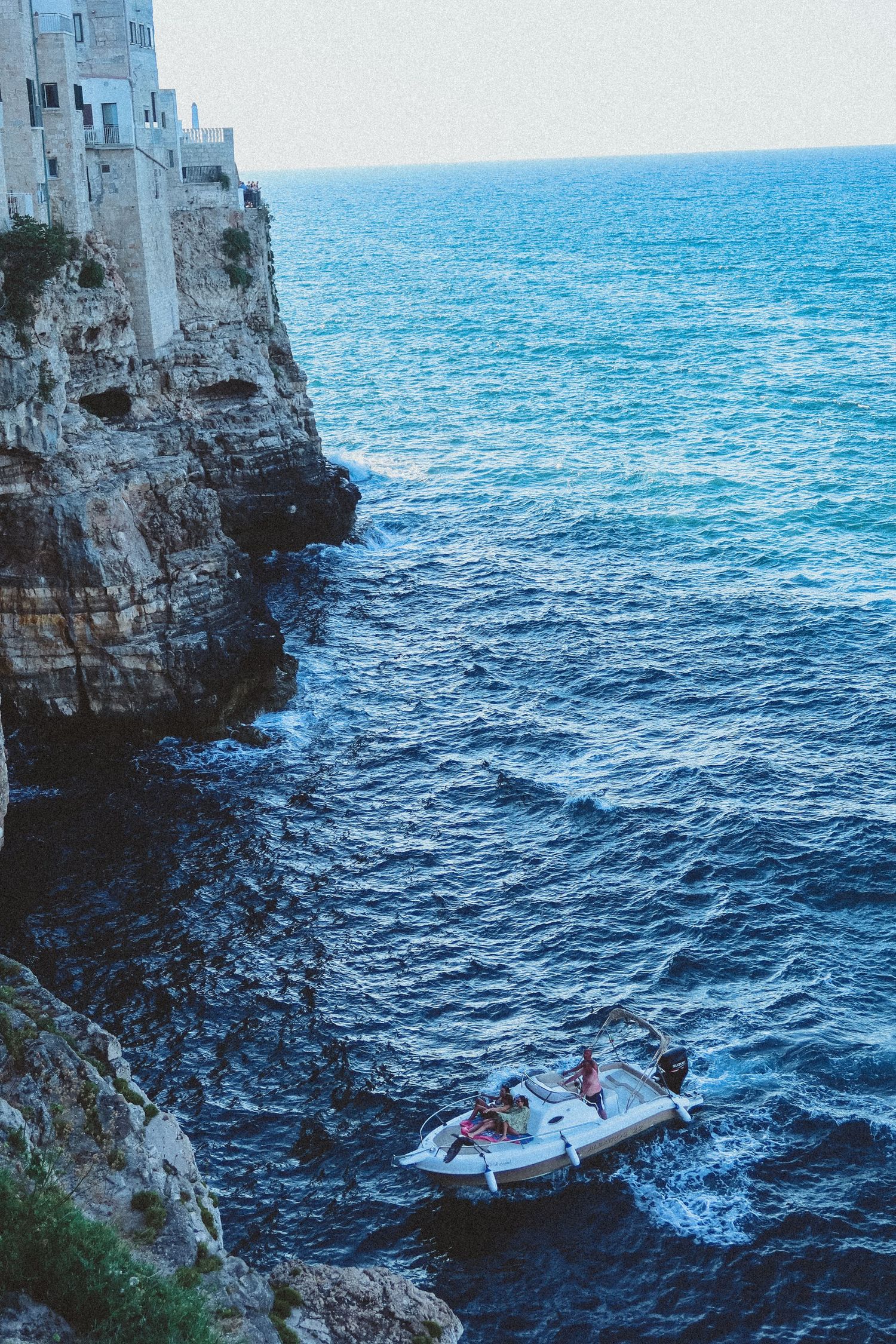 Dramatic coastal cliffs with boats navigating the blue Mediterranean waters below.