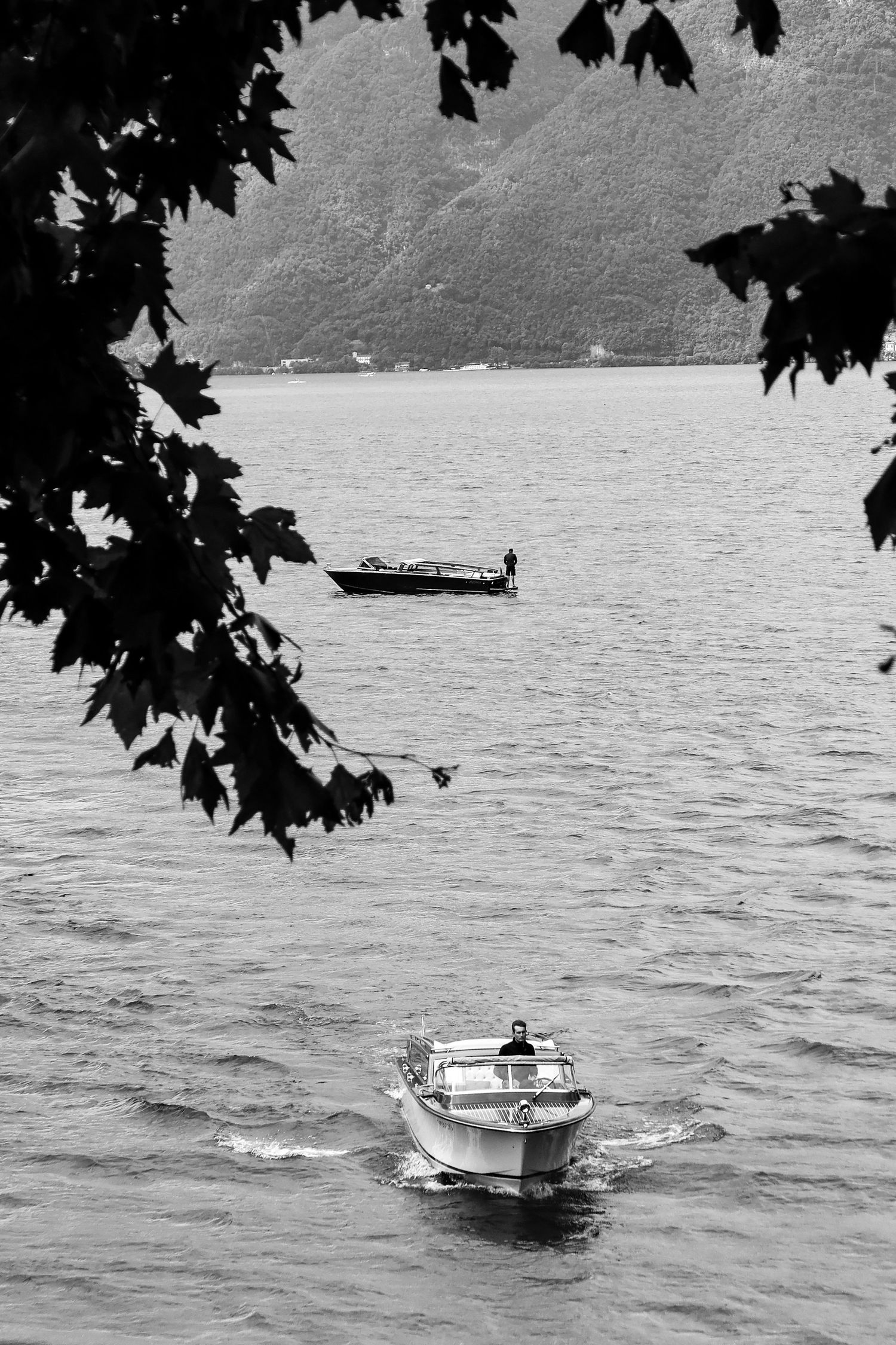 Small rescue boat traversing across a serene lake surrounded by mountains in black and white.