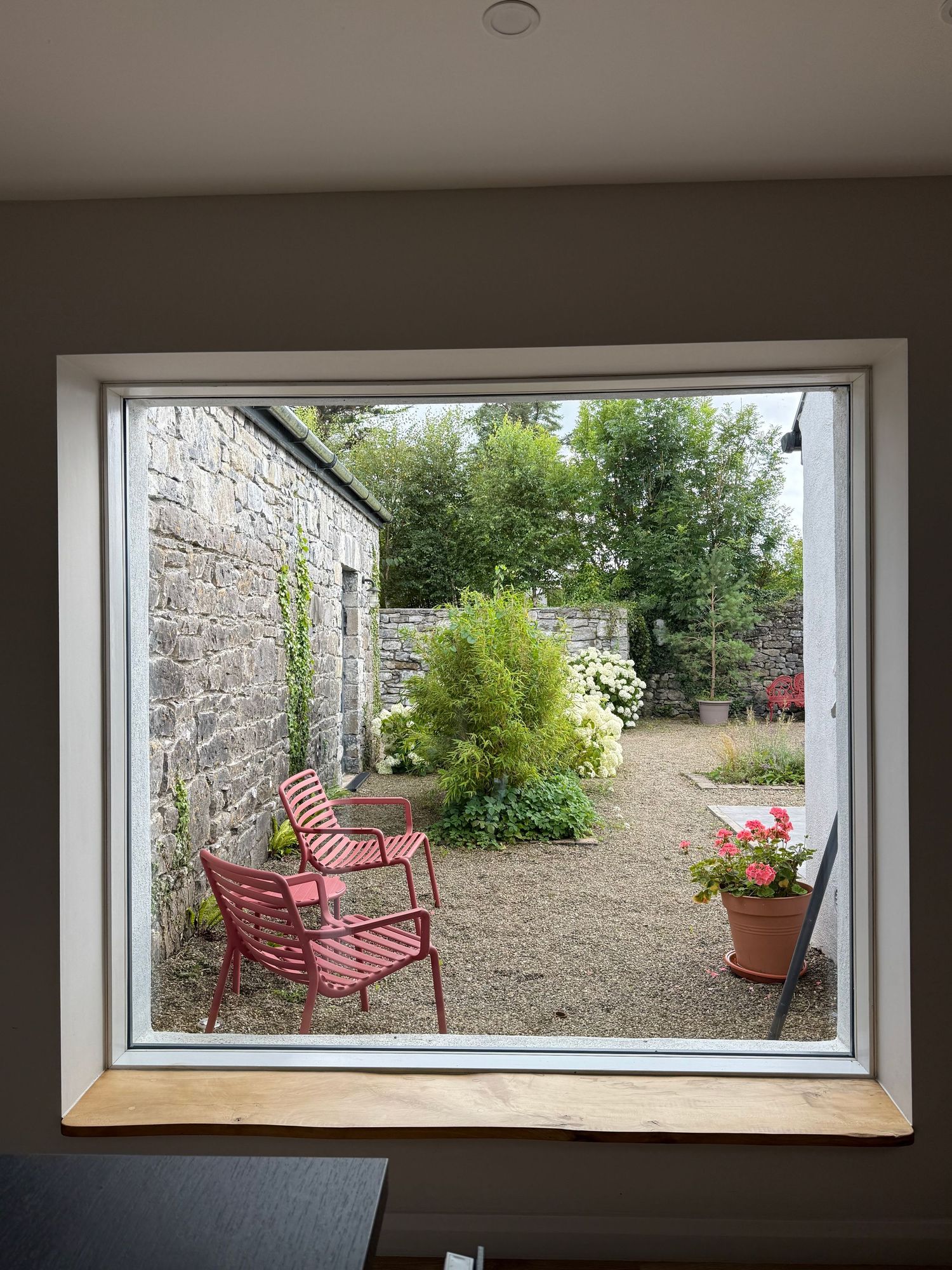 Series of panoramic windows in a stone wall reveal a tranquil garden scene with red benches and potted flowers.