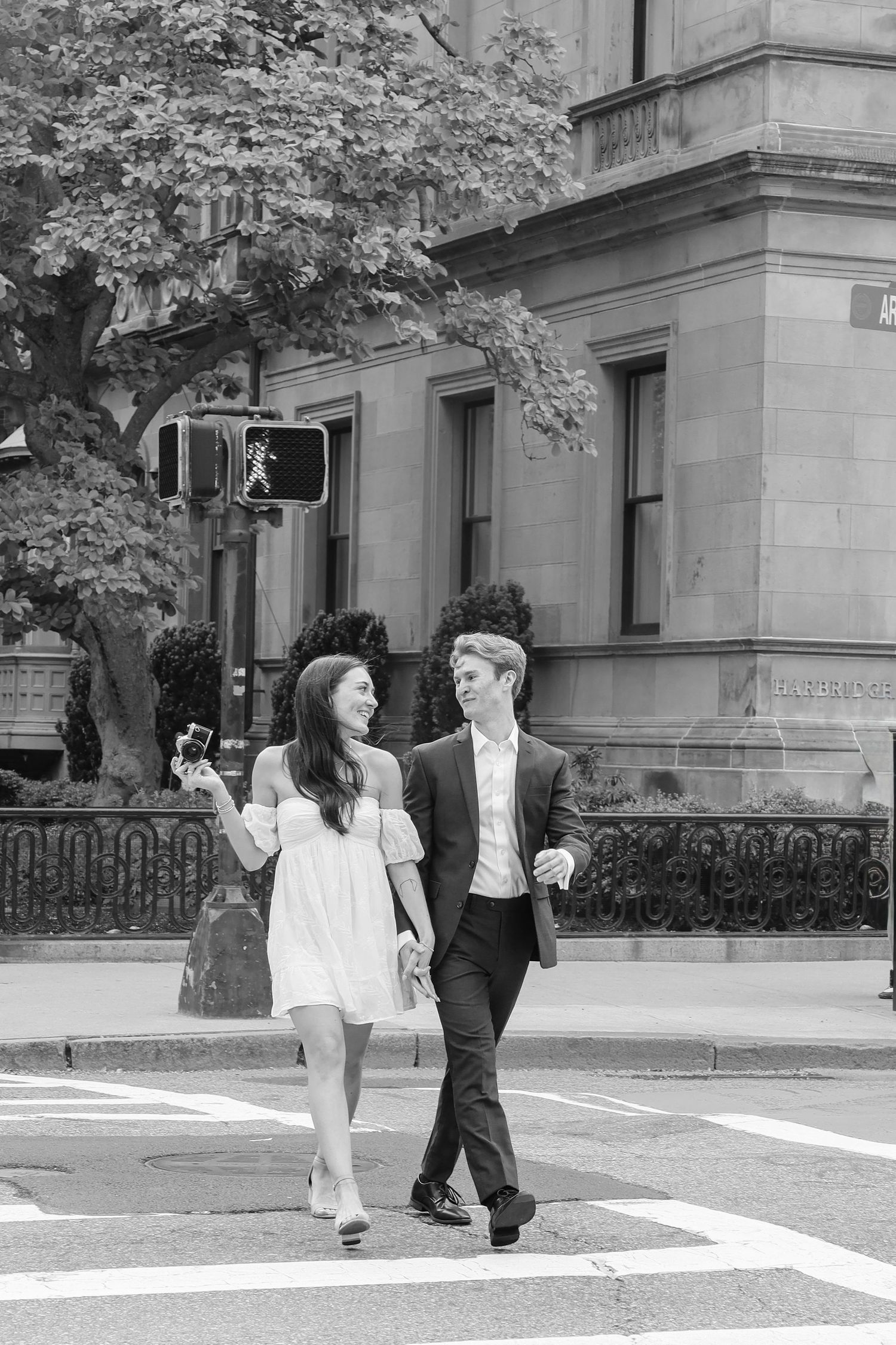 Black and white photo sequence of two people walking across a crosswalk near historic buildings.