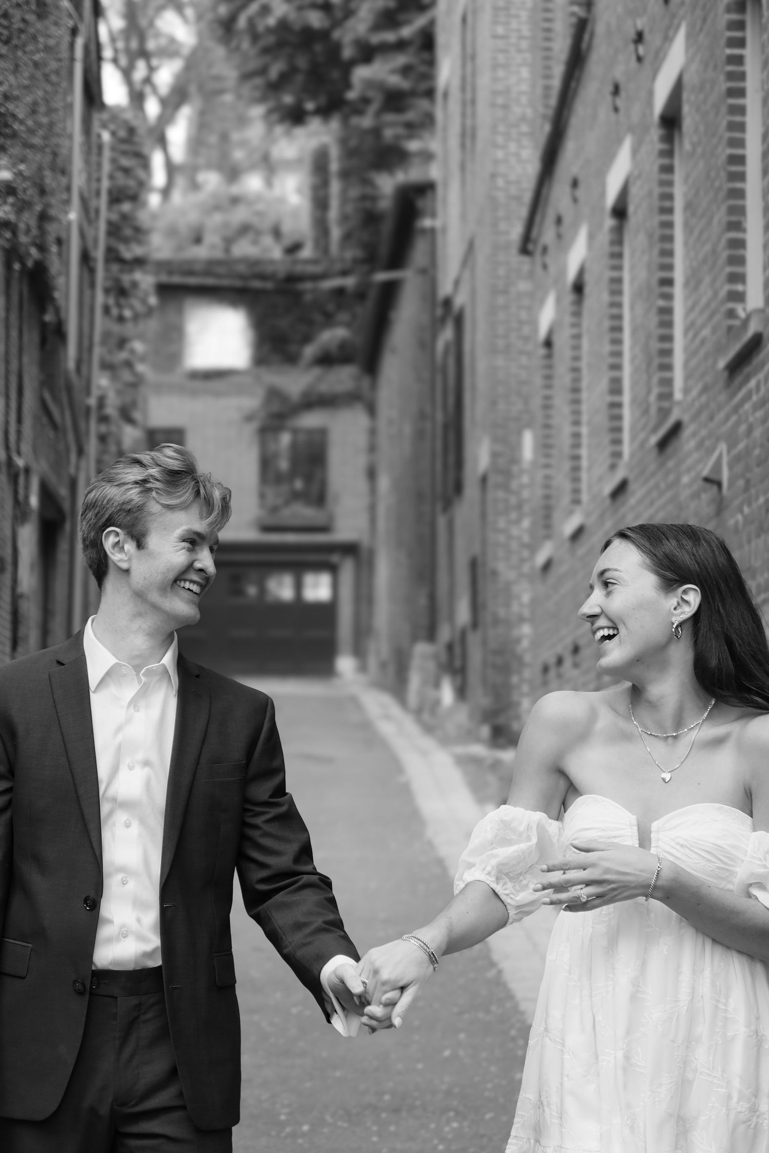 Couple shares candid laughing moments along a brick wall pathway.