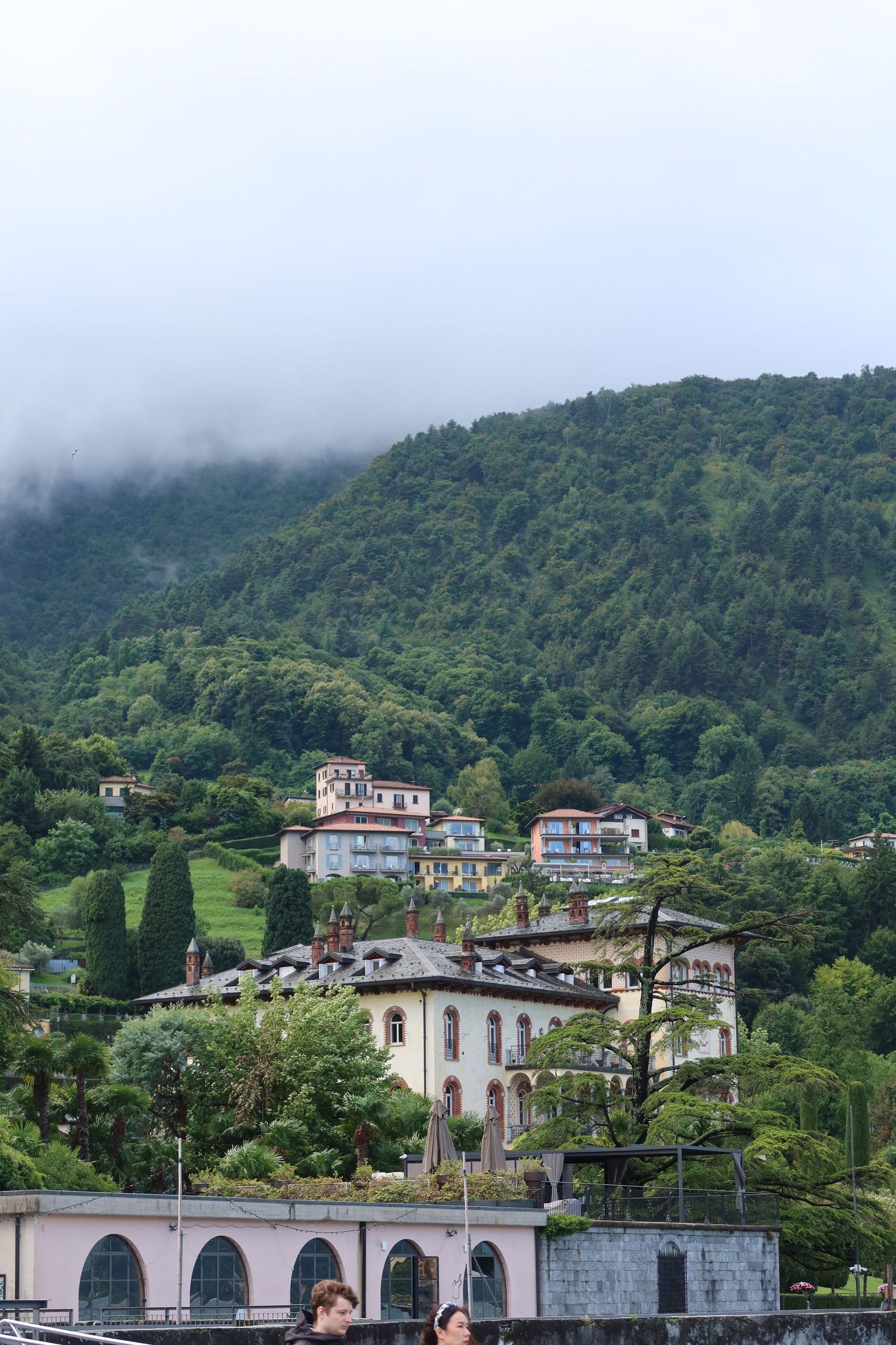 Lakeside Italian villa with white facade and arched colonnade beneath misty mountain slopes.