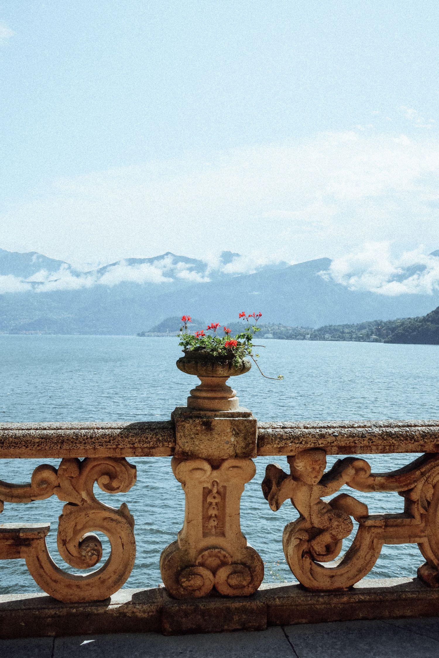 Decorative stone railing with carved faces and scrollwork against a scenic mountain lake backdrop.