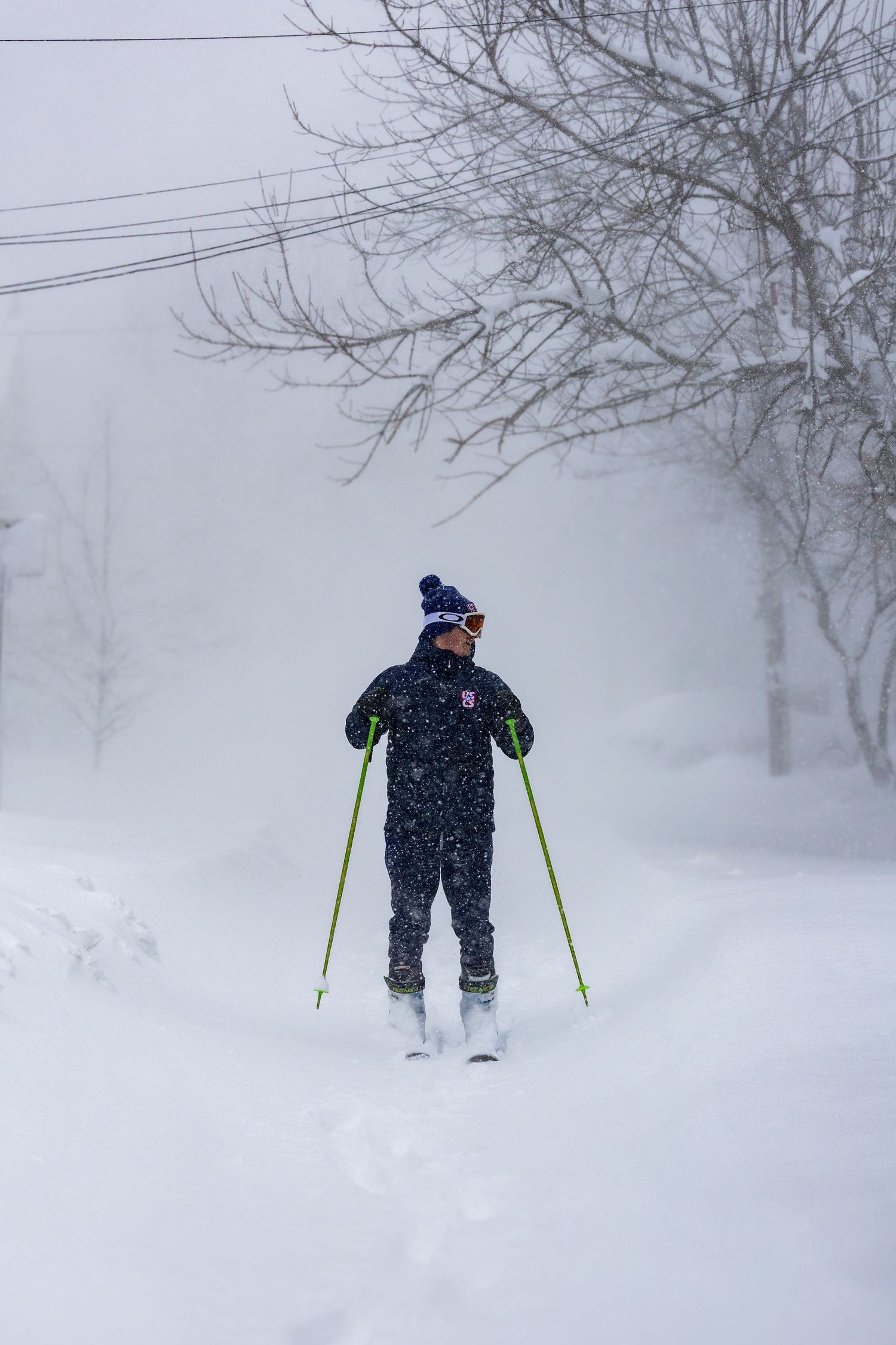 A skier stands in a snowy forest during heavy snowfall with fog creating a misty winter atmosphere.