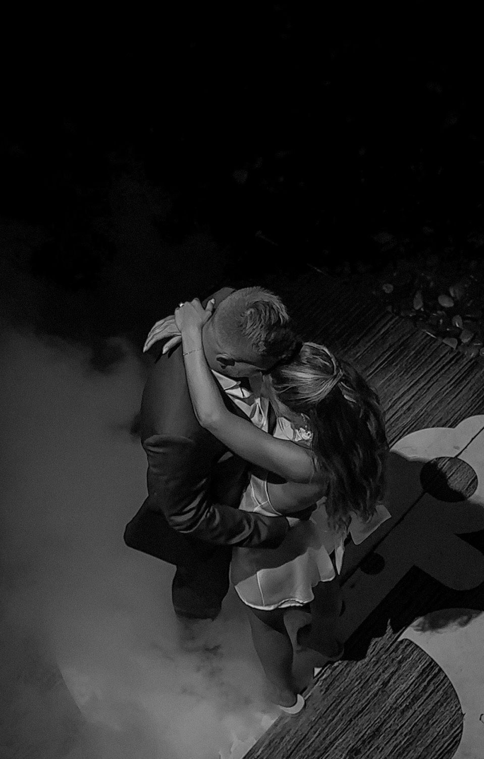 Couple performing an intimate dance sequence in dramatic lighting and fog on a wooden floor.