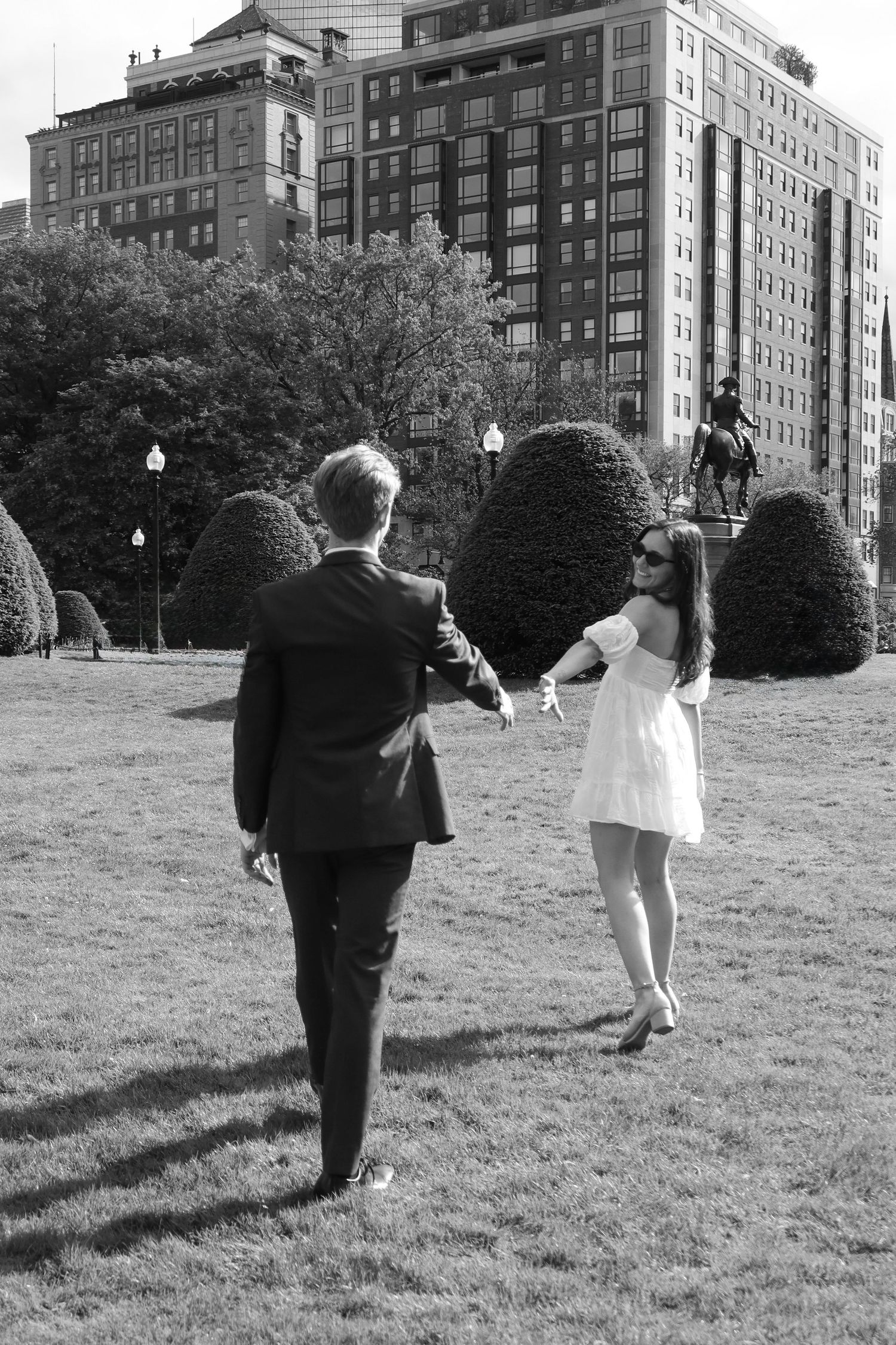 A couple dances on a lawn with historic apartment buildings in the background.