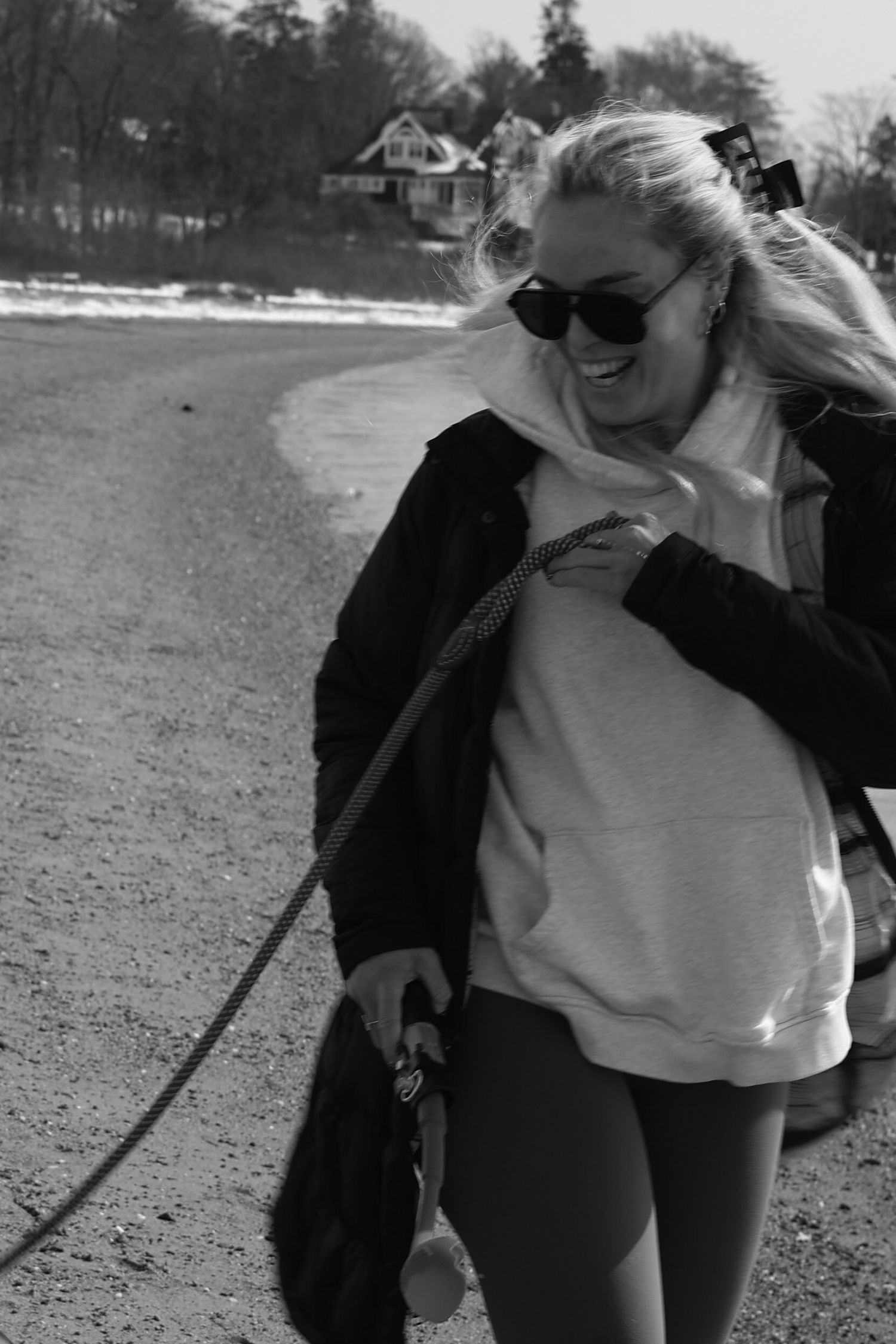 A person in a black jacket and white shirt laughs while walking outdoors on a sunny day.