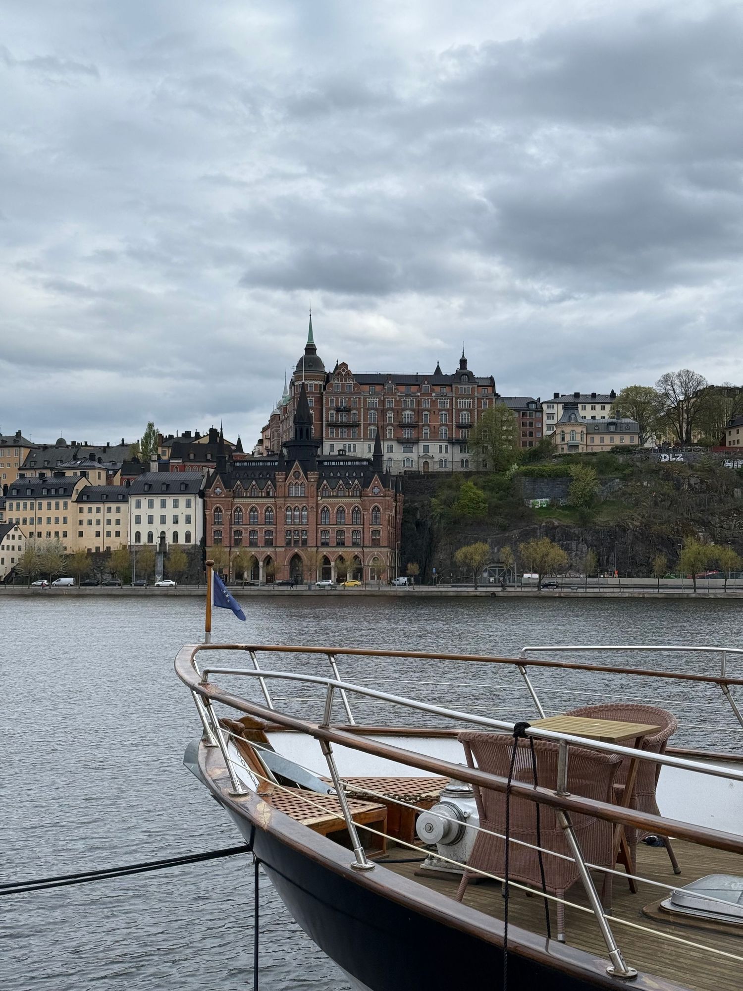 Classic wooden tour boats moored at a dock with historic buildings along Stockholm's waterfront under cloudy skies.