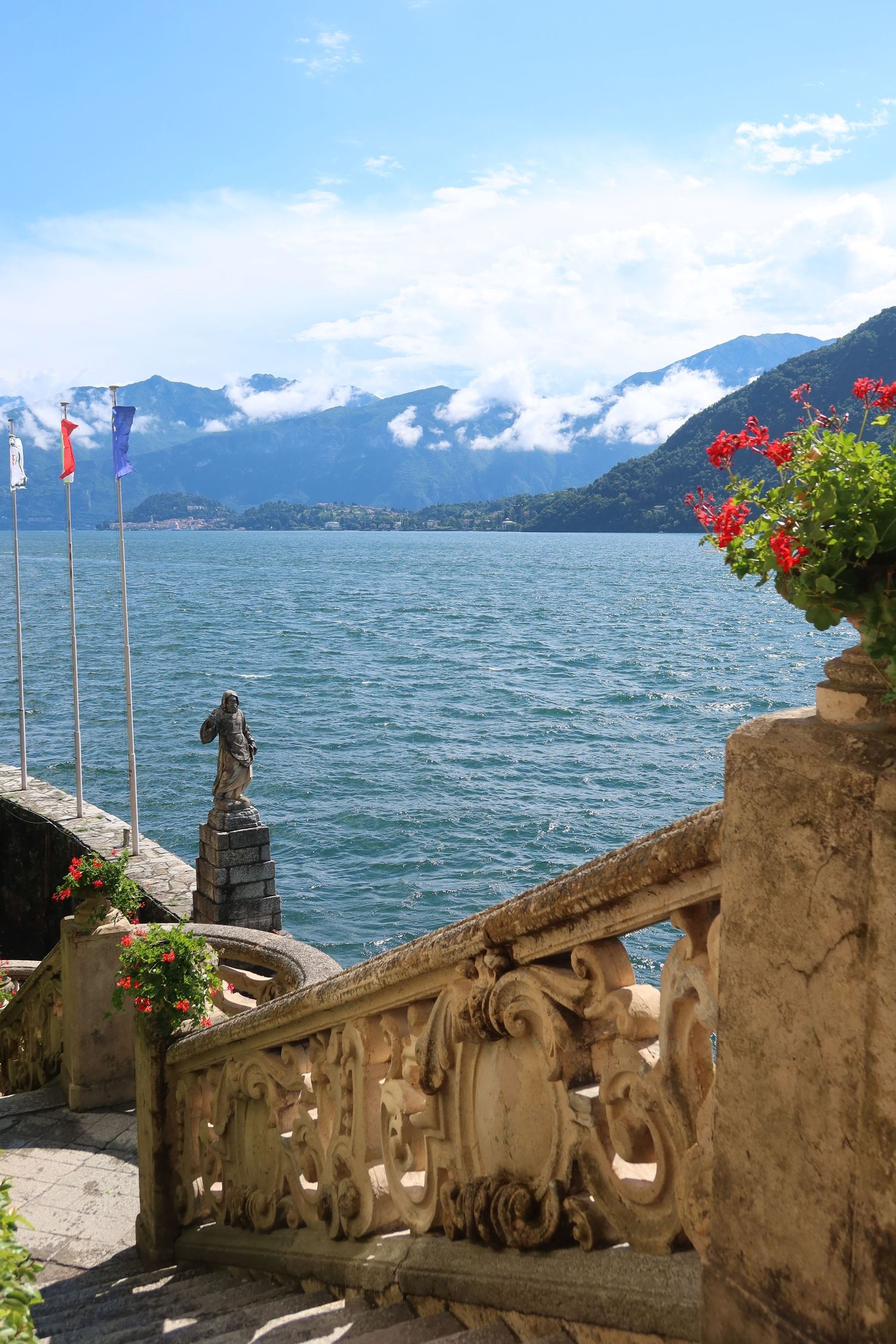 Historic stone balustrade with red flowers overlooking a scenic mountain lake view.