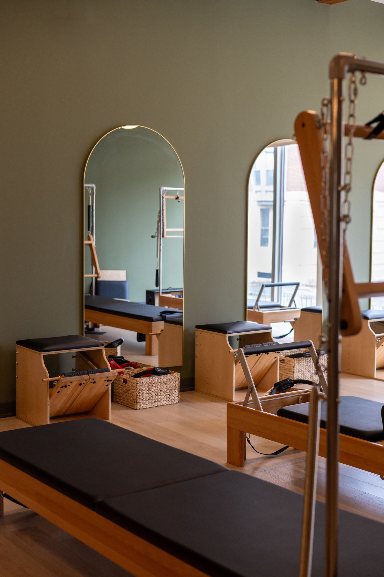 Pilates studio interior showing wooden reformer equipment and mirrors in a serene, naturally lit space.