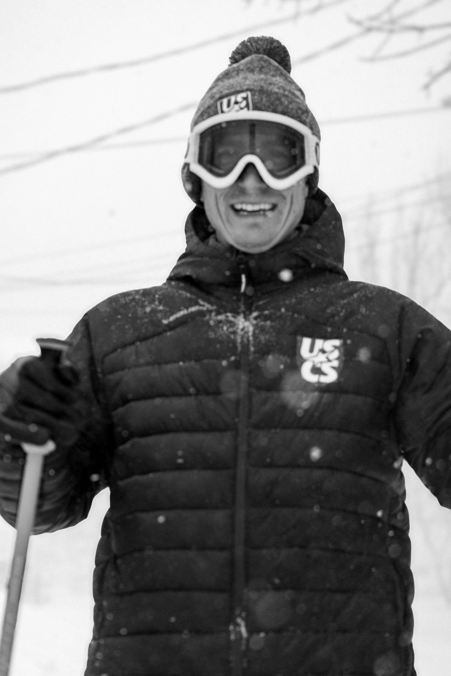 A skier in black winter gear and goggles stands in snowy conditions on the slopes.