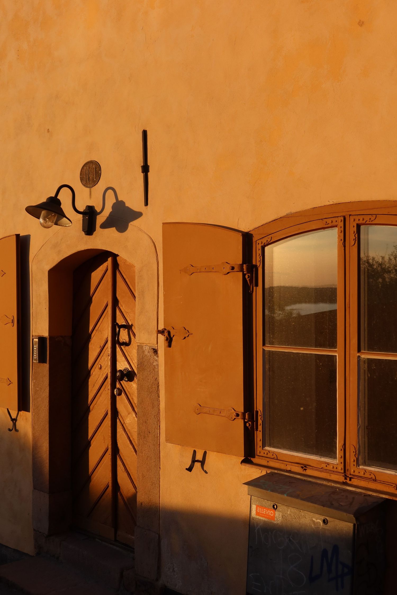 Row of arched windows casting dramatic shadows on orange wall during sunset.