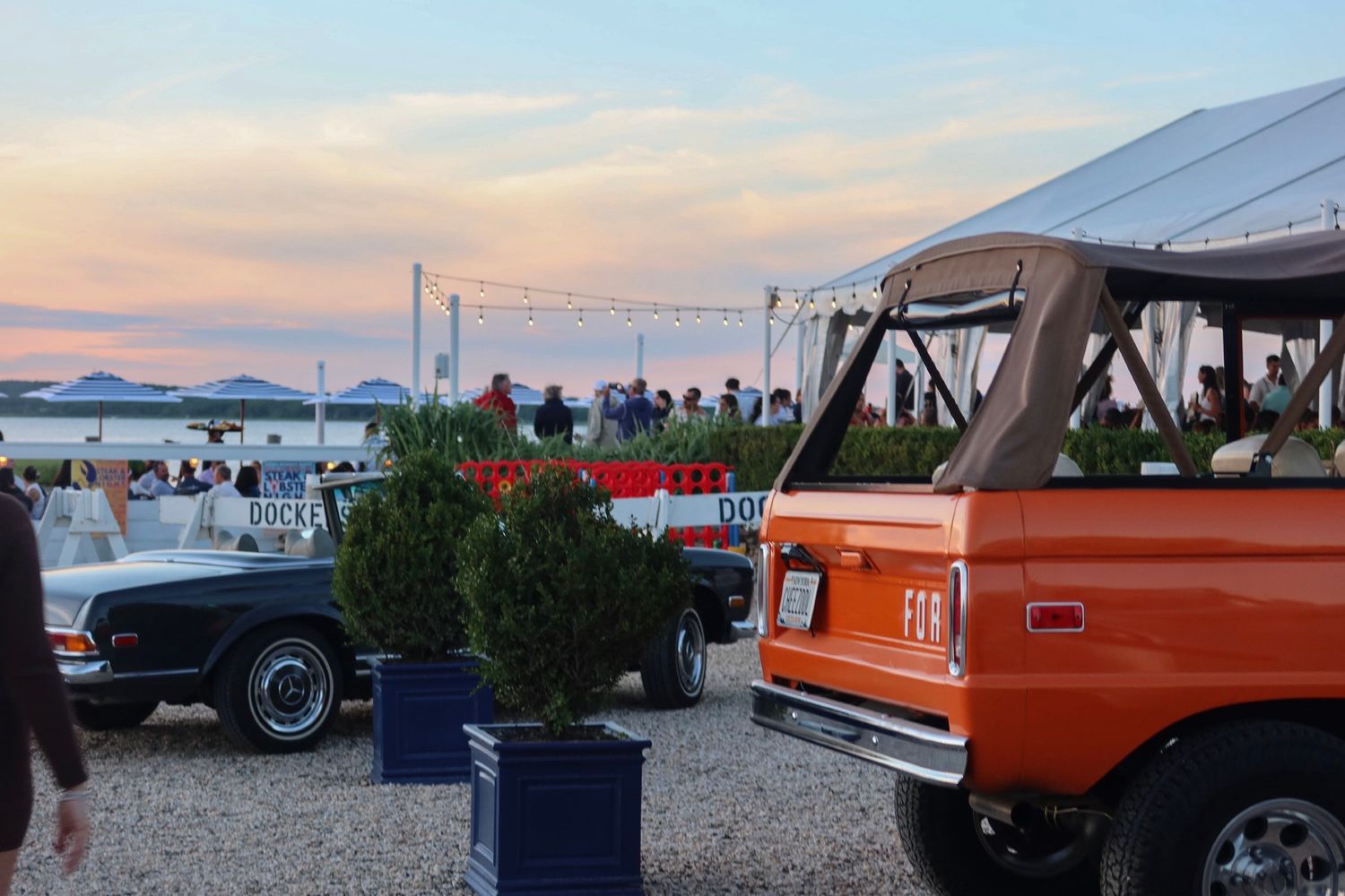 Classic orange vintage cars lined up at an outdoor event during sunset.