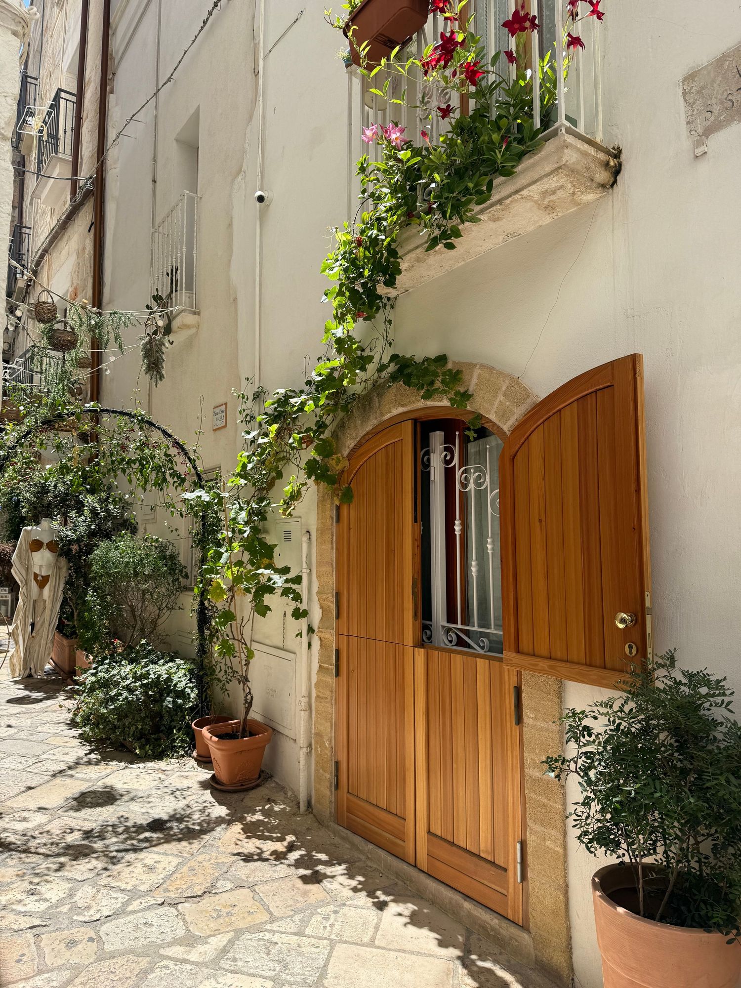 Mediterranean style courtyard with wooden doors and climbing plants along white stone walls.