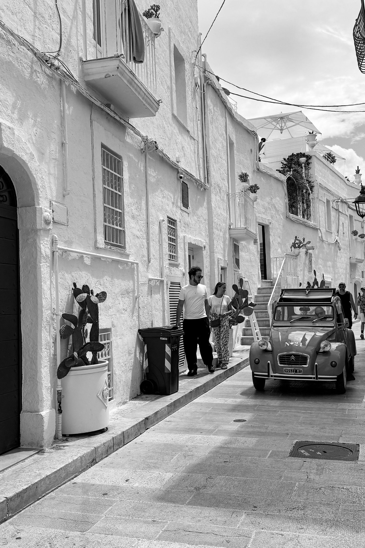Vintage black and white photograph of narrow Mediterranean street with classic cars.
