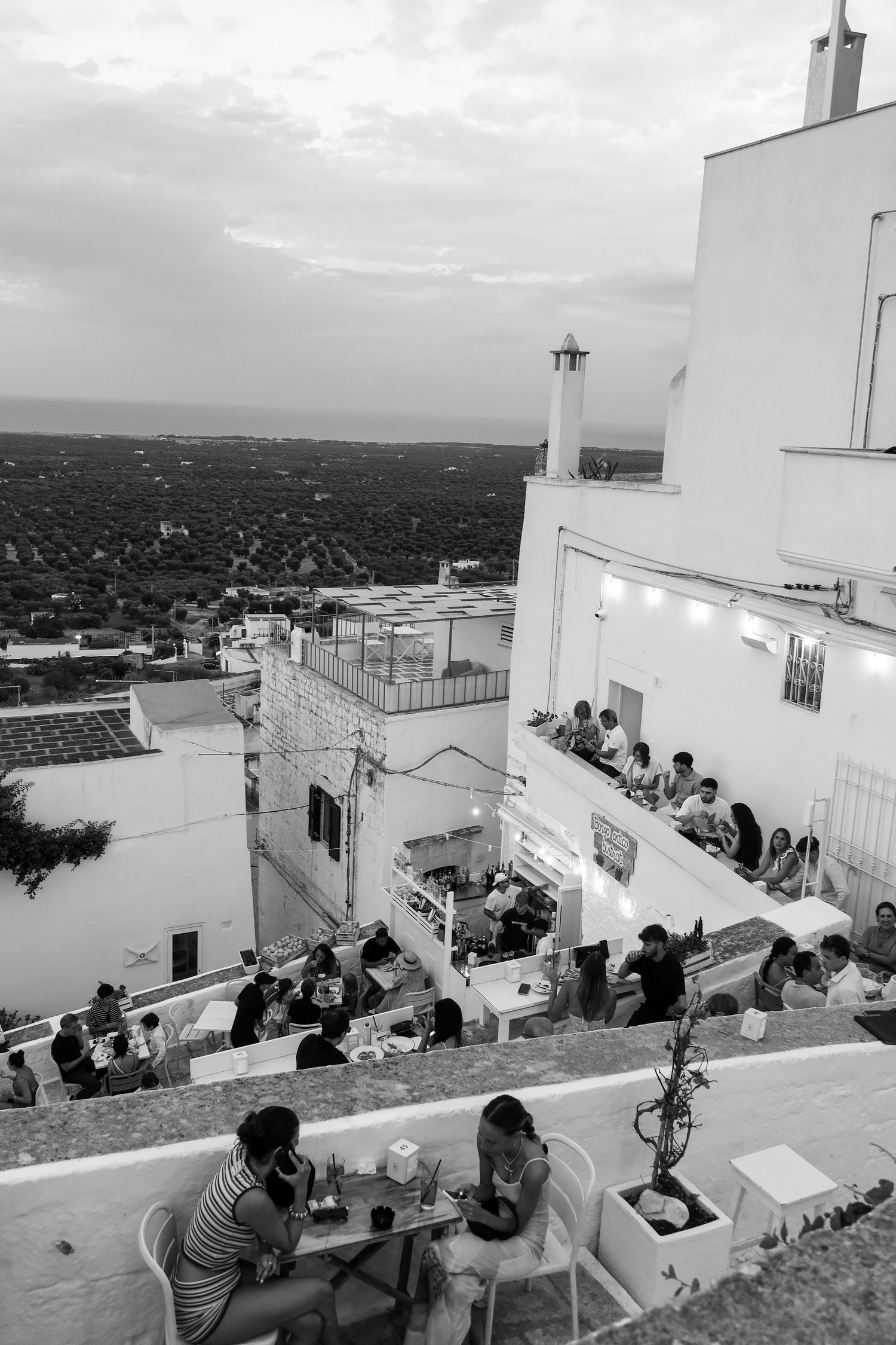 Rooftop terrace overlooking a coastal town with diners enjoying the panoramic view at sunset.