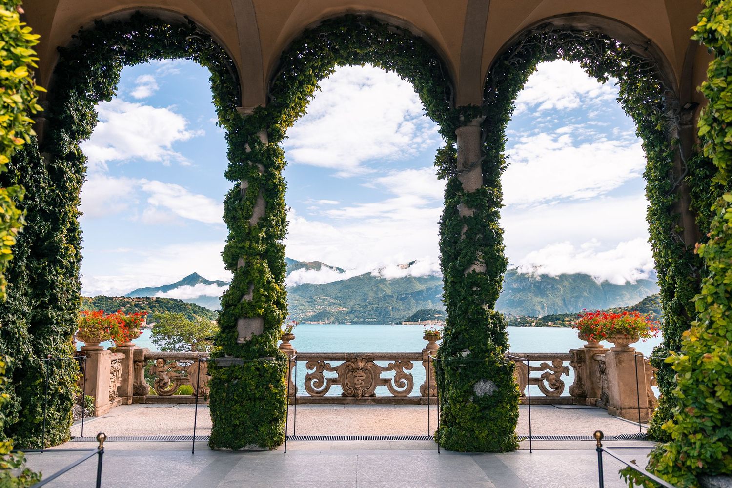 Scenic archway covered in ivy overlooking a lake and mountain landscape.