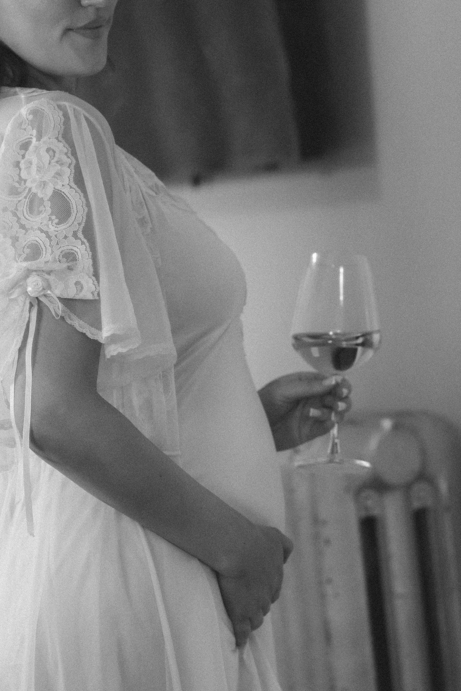 Pregnant woman in white lace dress holding wine glass, black and white photo.