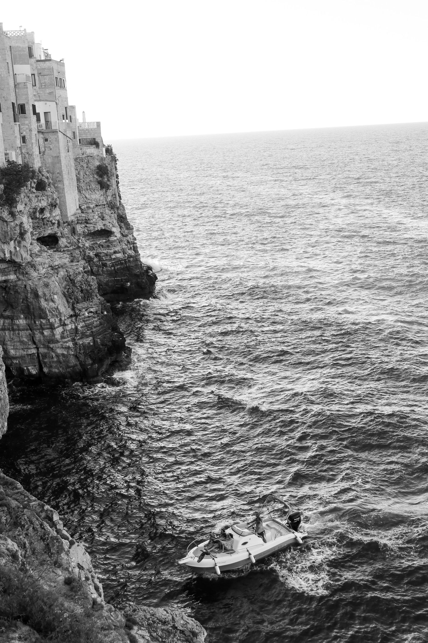 Black and white photograph of boats against dramatic limestone cliffs over the sea.