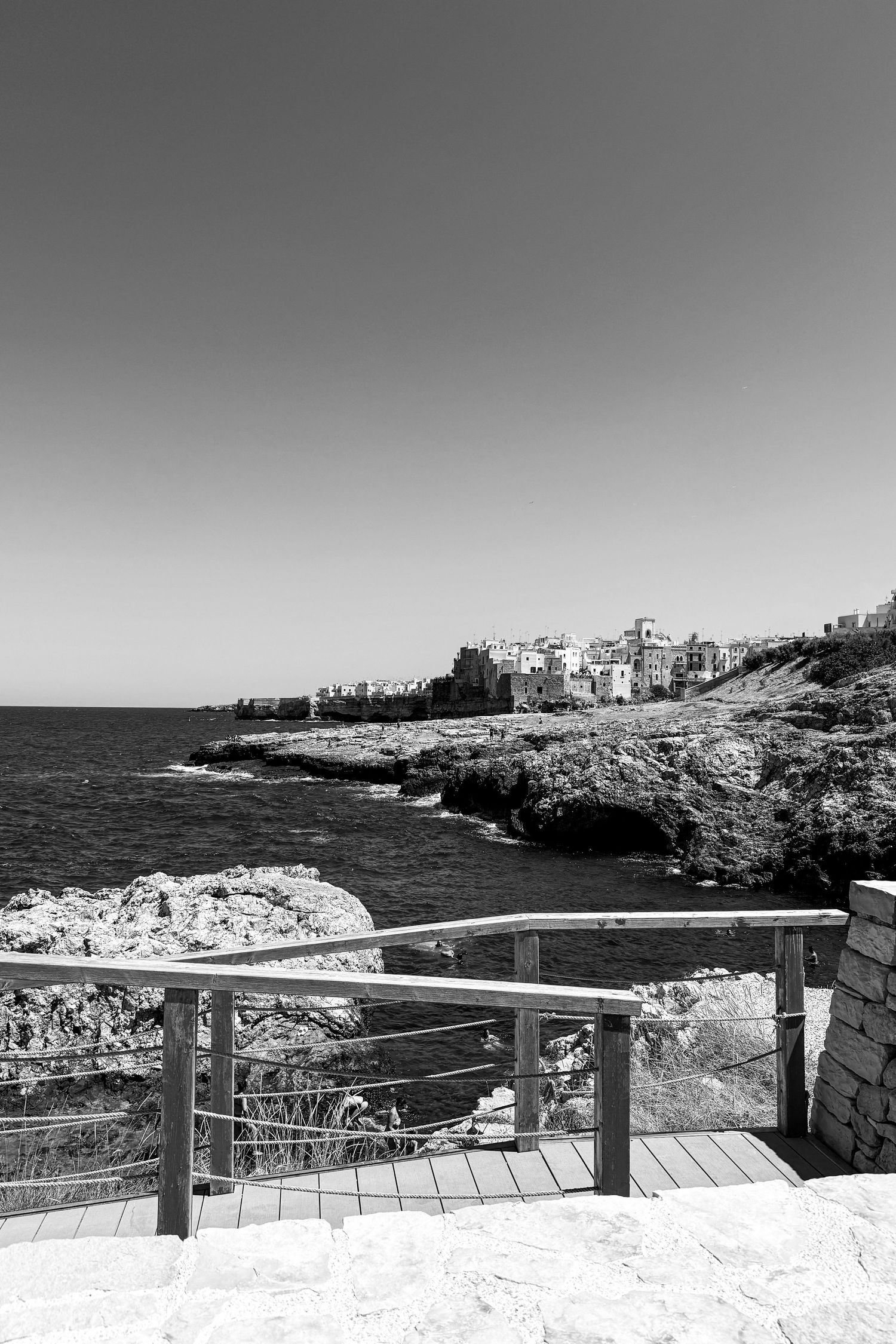Black and white coastal landscape with viewing terrace overlooking rocky Mediterranean shoreline.