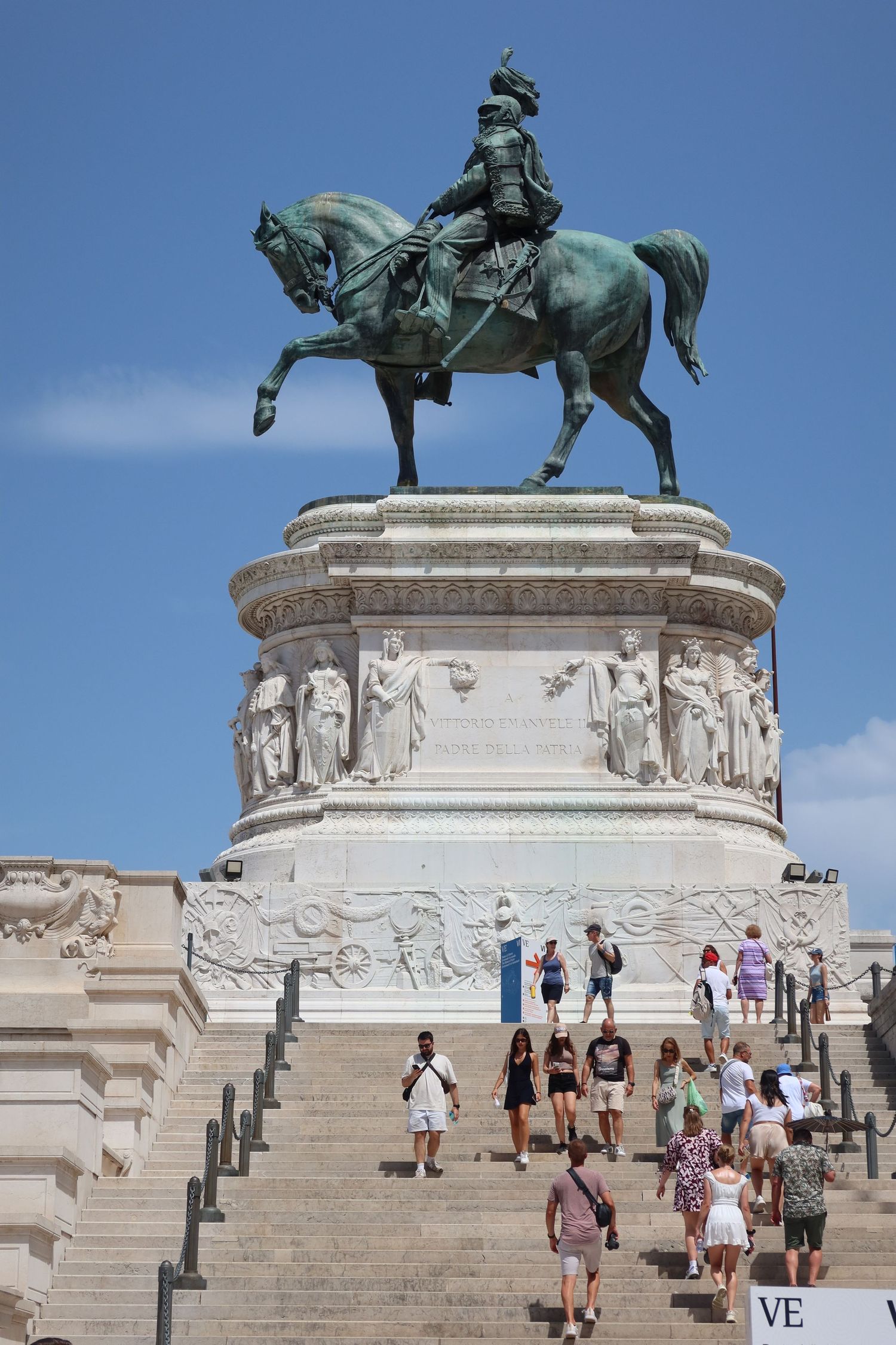 Bronze equestrian statue on grand white marble steps with visitors climbing the monument.