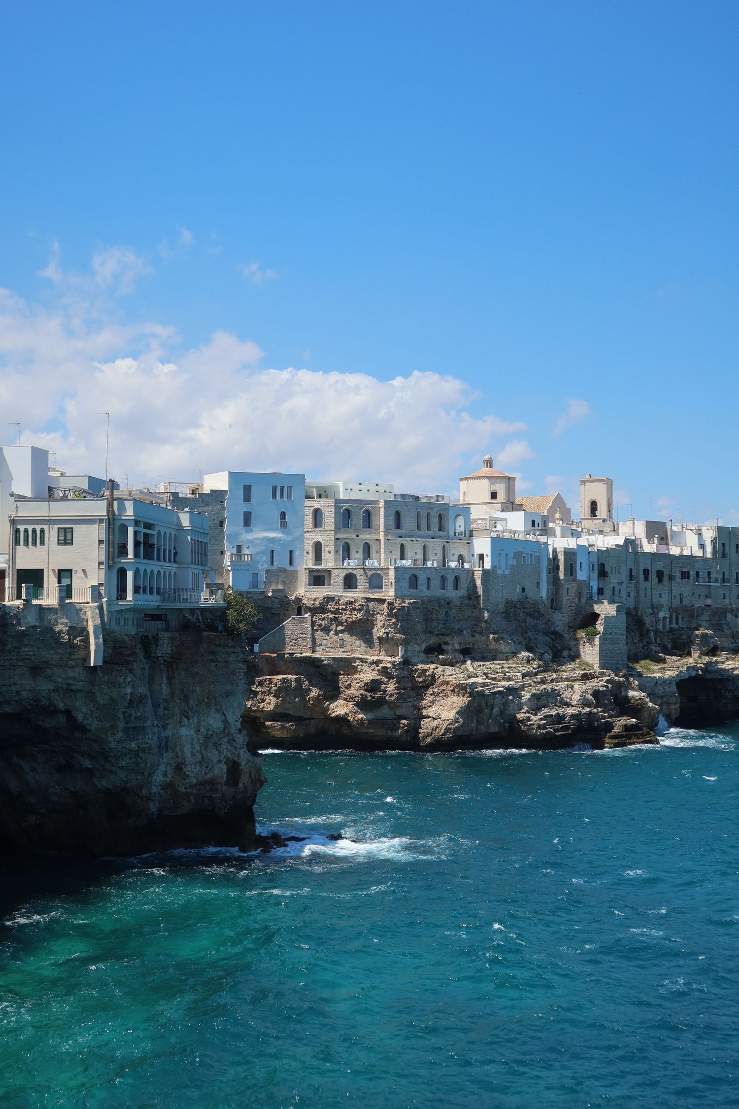 White coastal buildings perched on cliffs above turquoise Mediterranean waters.