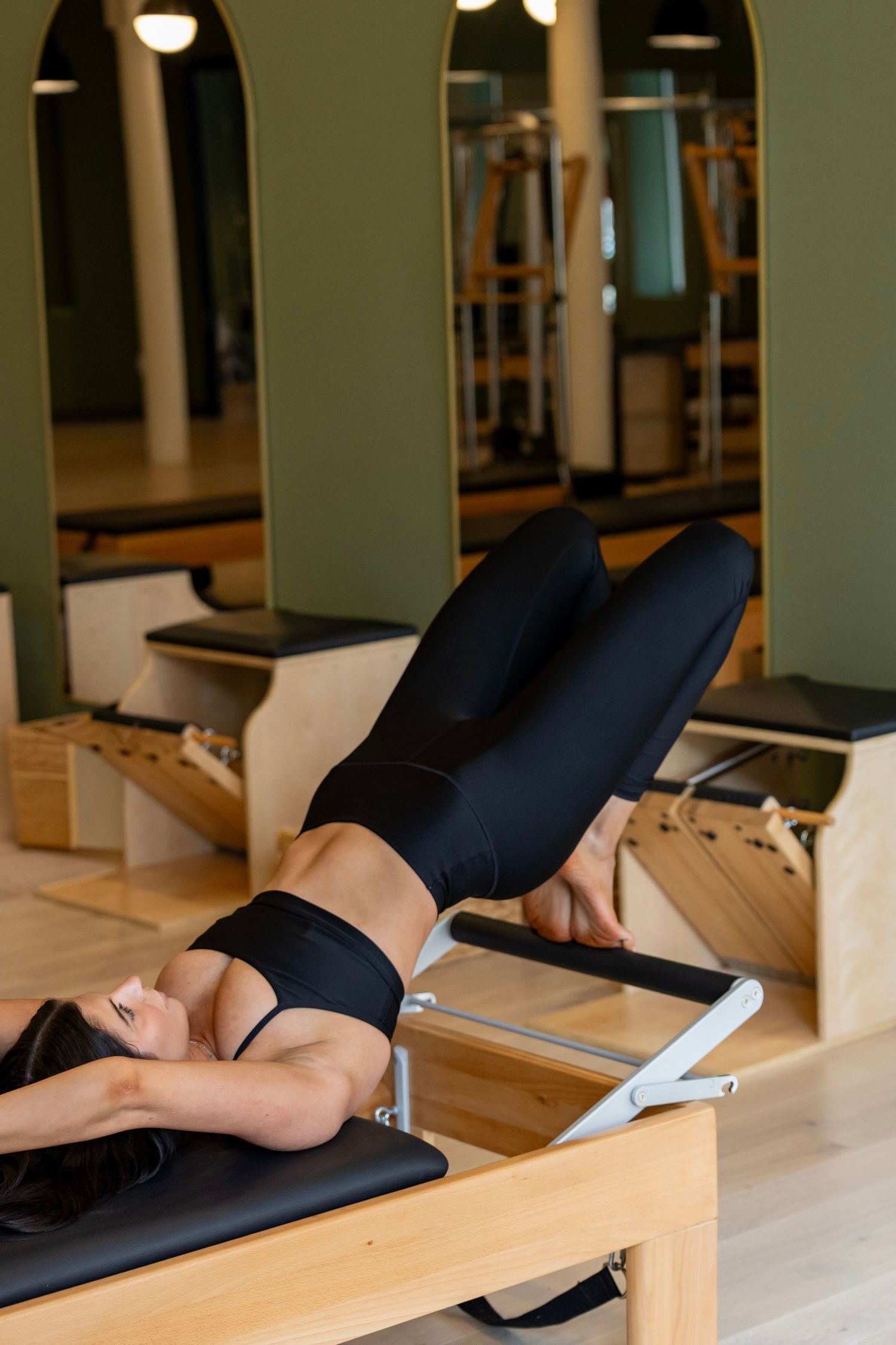 Side view of Pilates reformer exercise demonstrating proper form on wooden equipment.