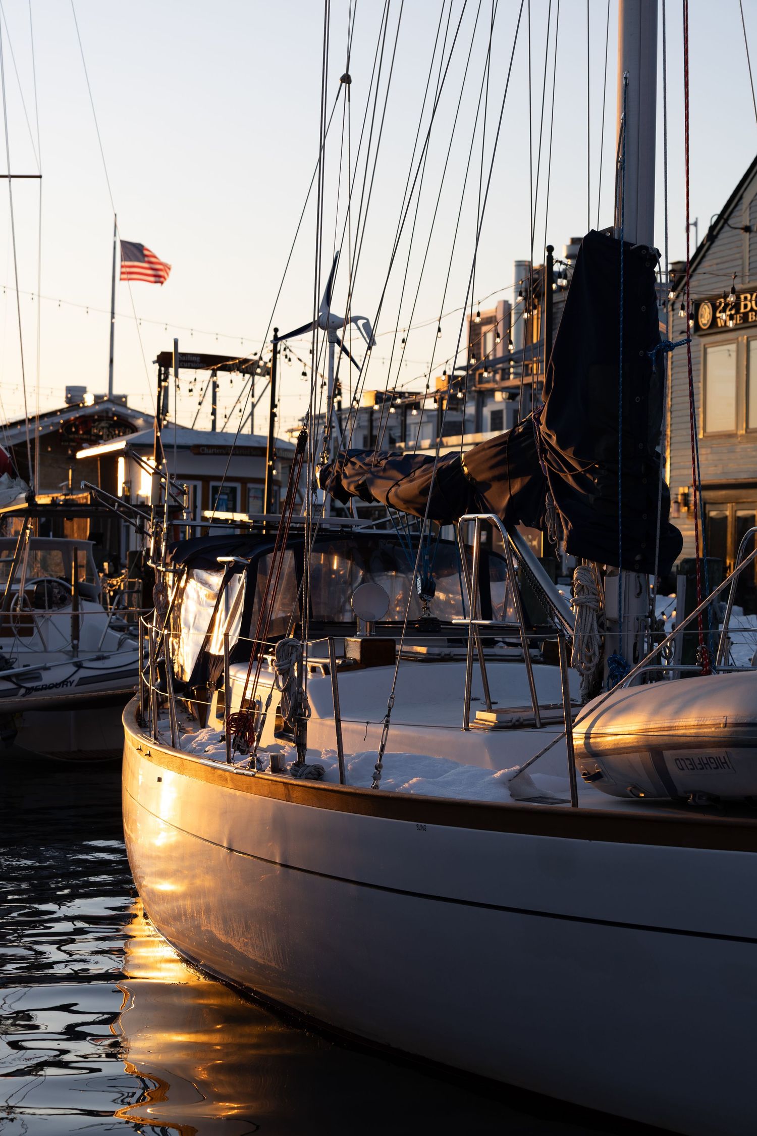Sailboats docked at a marina during golden hour with warm sunlight reflecting off their hulls and masts.