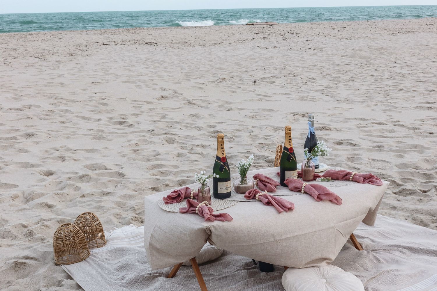 Elegant beach picnic setup with white cushions and blankets laid out on pristine sand.