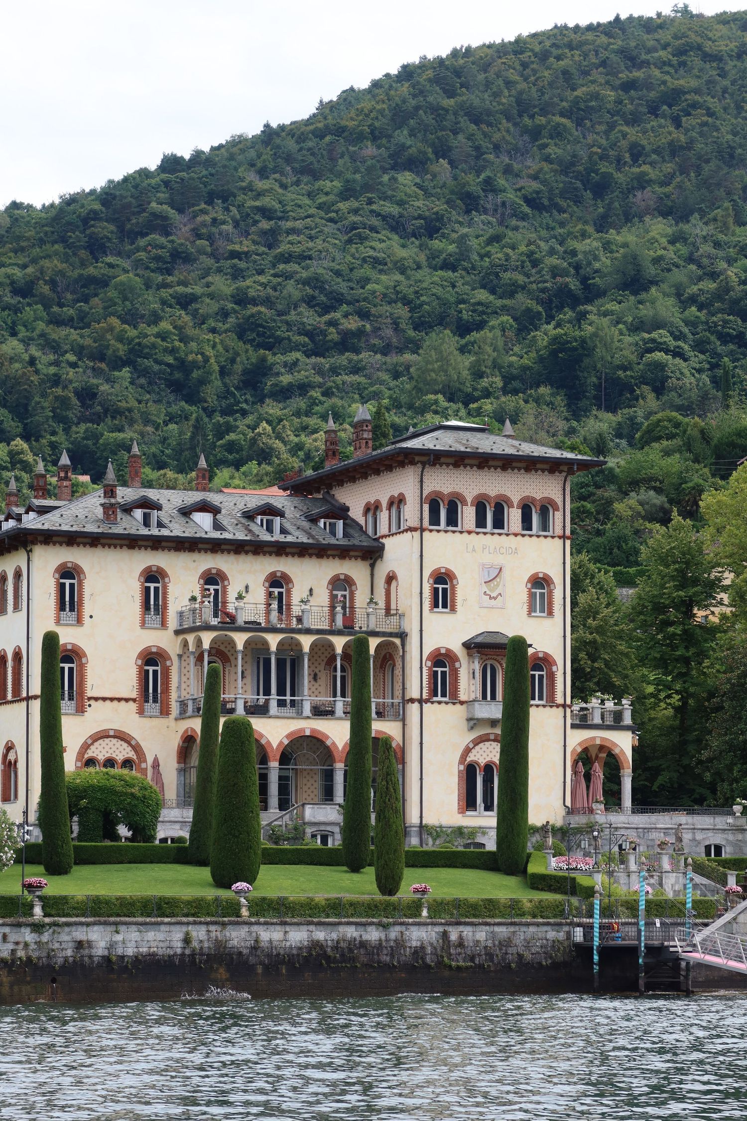 Elegant Italian villa with cypress trees and manicured gardens situated on Lake Como's shoreline.