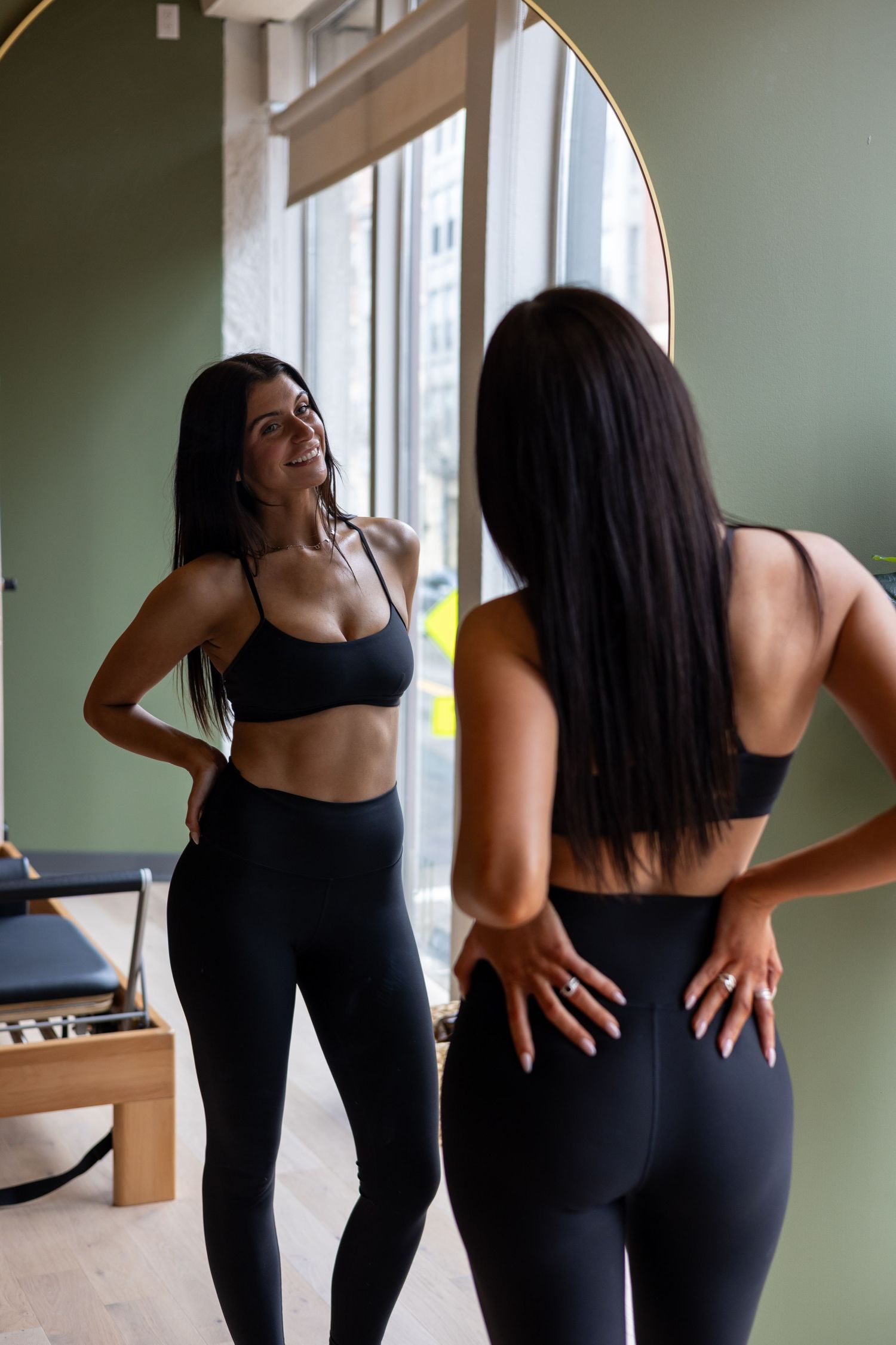 Athletic woman in black workout attire checking her form in a mirror during an indoor fitness session.
