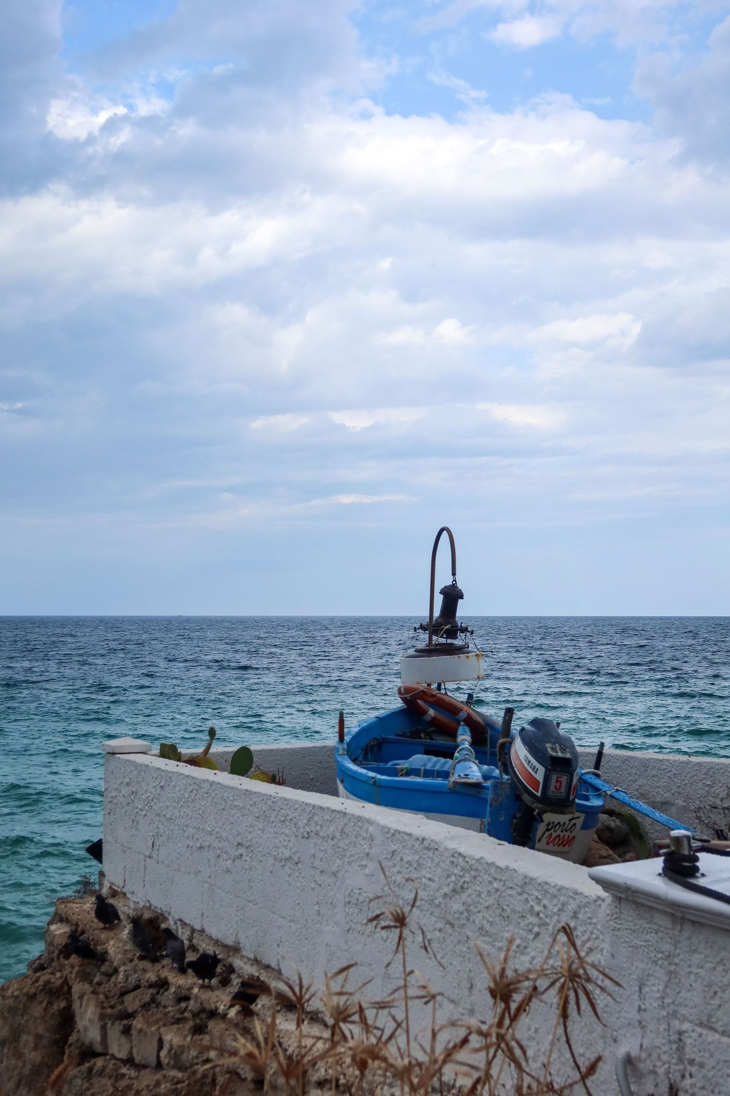 Small fishing boats on the horizon of a blue Mediterranean sea against cloudy skies.