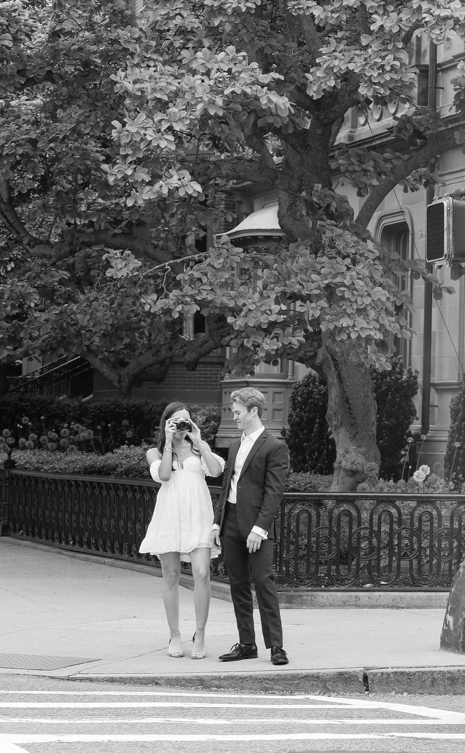 Black and white sequence of two people crossing a street near historic stone buildings.