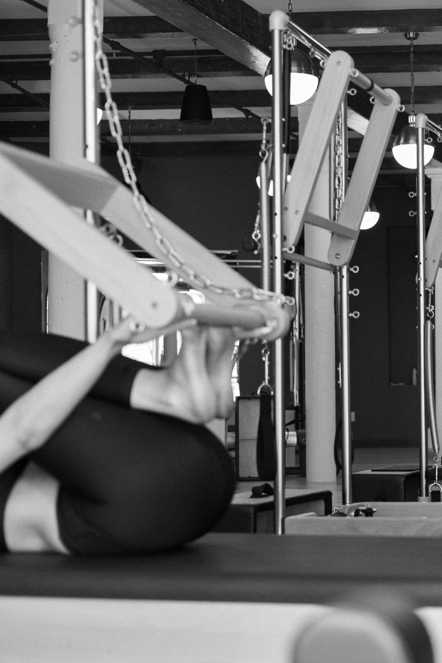 Black and white image of exercise equipment in a gym showing pilates reformer machines with straps and pulleys.