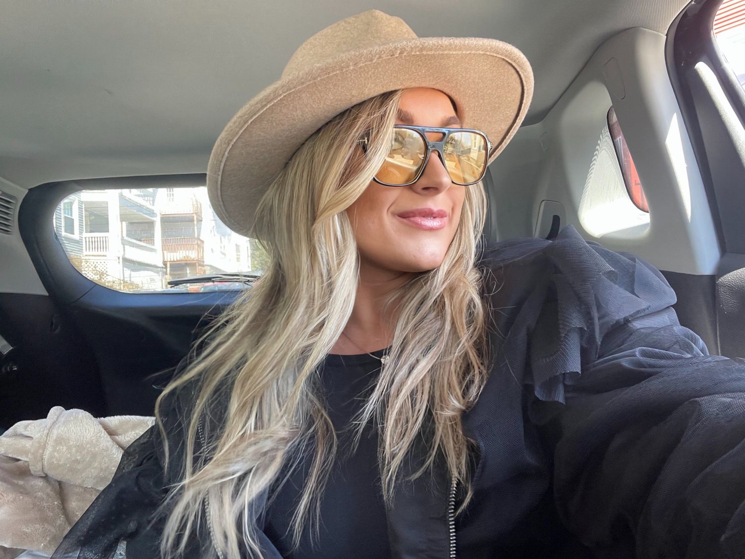 A person wearing a wide-brimmed sun hat sits in a car with sunlight streaming through the window.
