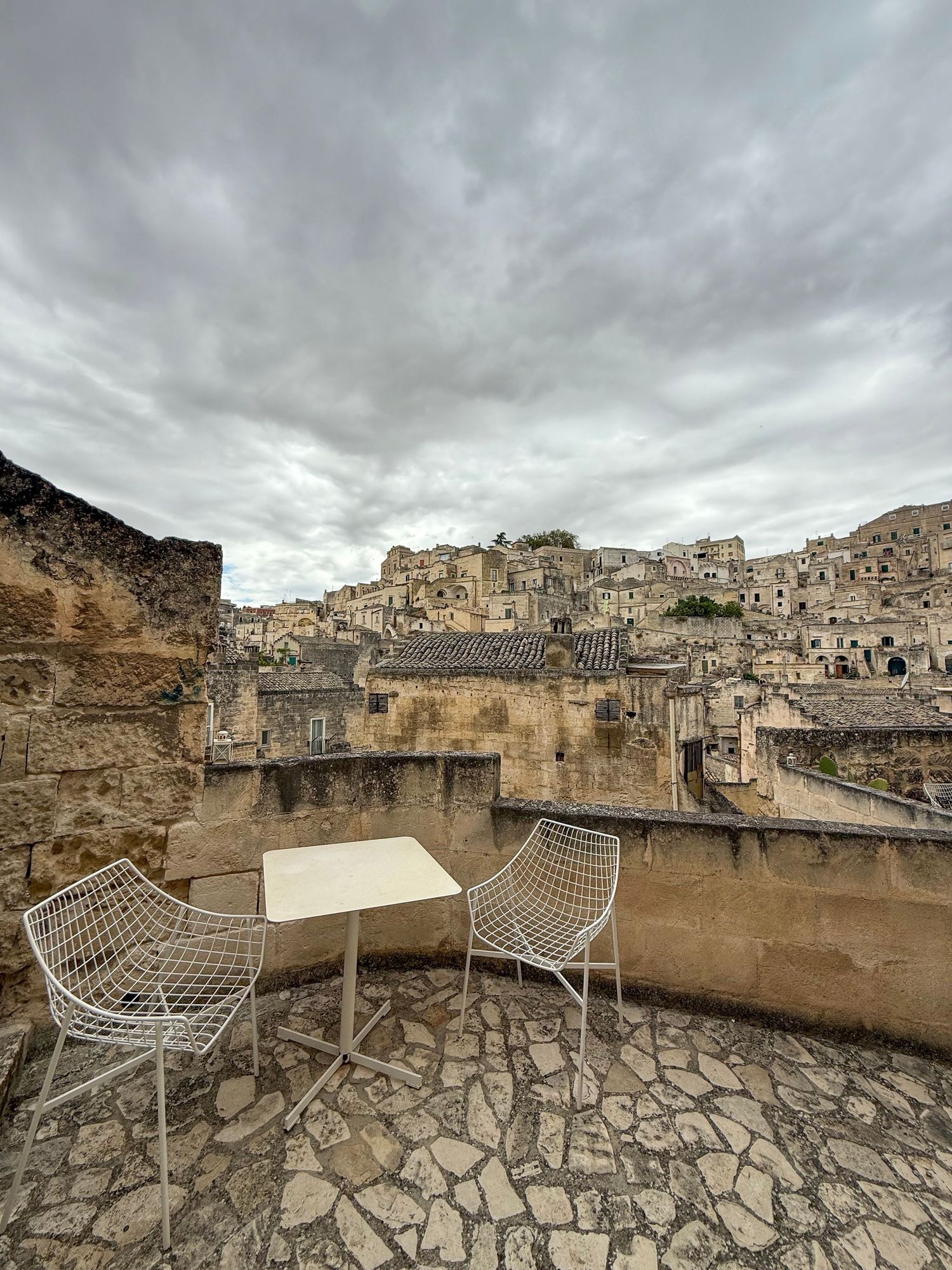 A stone terrace with modern chairs overlooking ancient buildings in Matera, Italy.