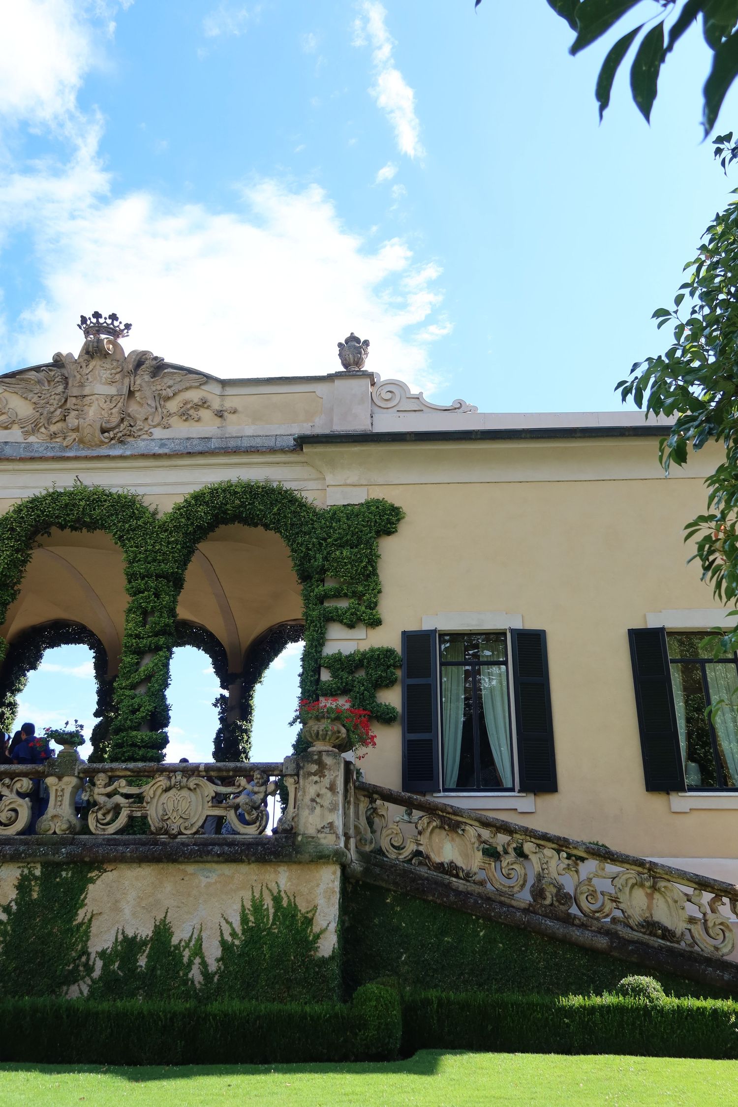 Yellow villa with ivy-covered arches and ornate stone balustrade in Mediterranean style.