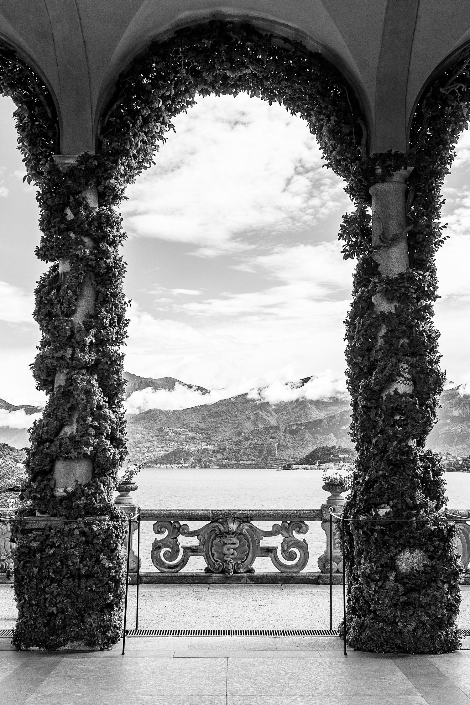 Elegant colonnade with ivy-covered pillars framing a panoramic lake and mountain view.