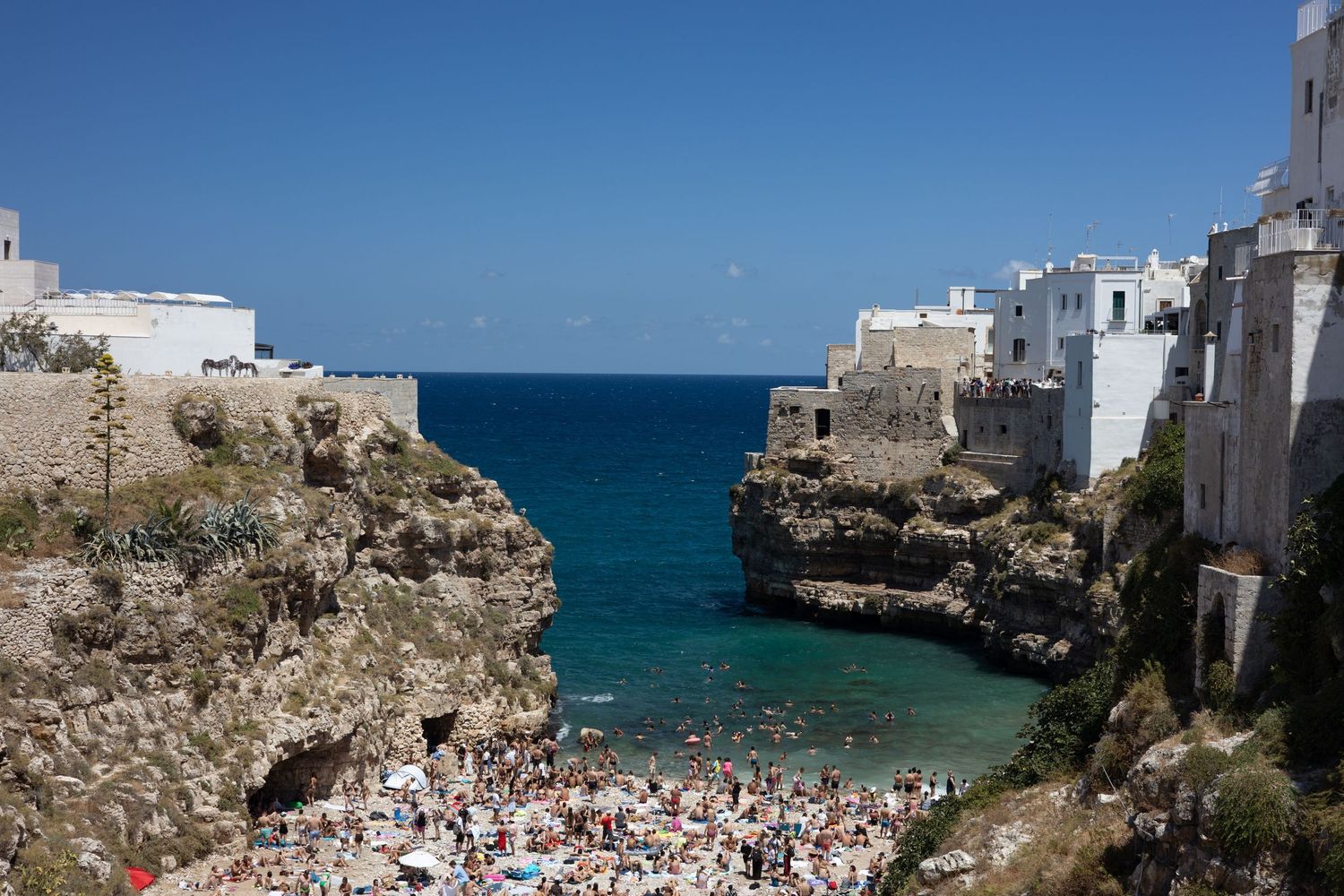 Coastal panorama of white buildings and beach crowds along the turquoise Mediterranean Sea.