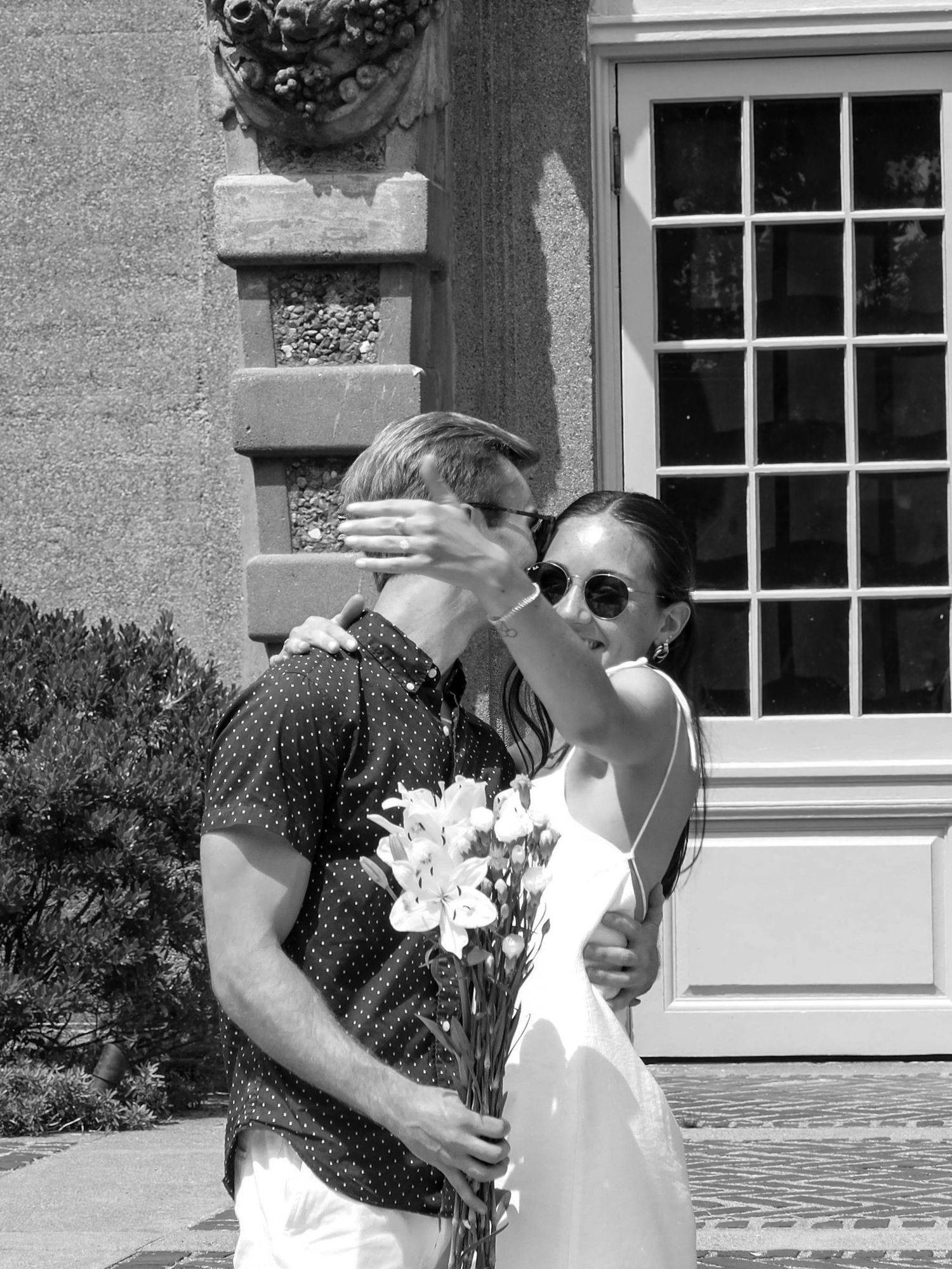 Black and white photo of a romantic moment outside a building with windows.