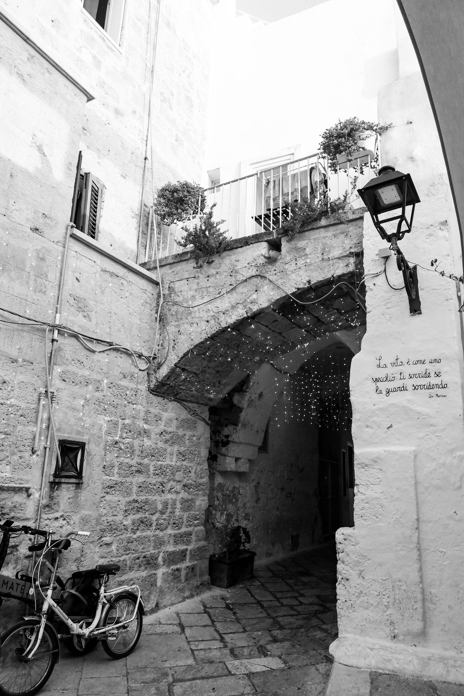 Black and white photograph of a stone archway and steps in an old Mediterranean village.