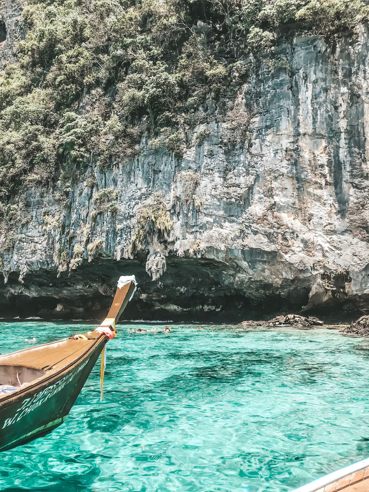 Traditional Thai longtail boat floating on turquoise waters near dramatic limestone cliffs.