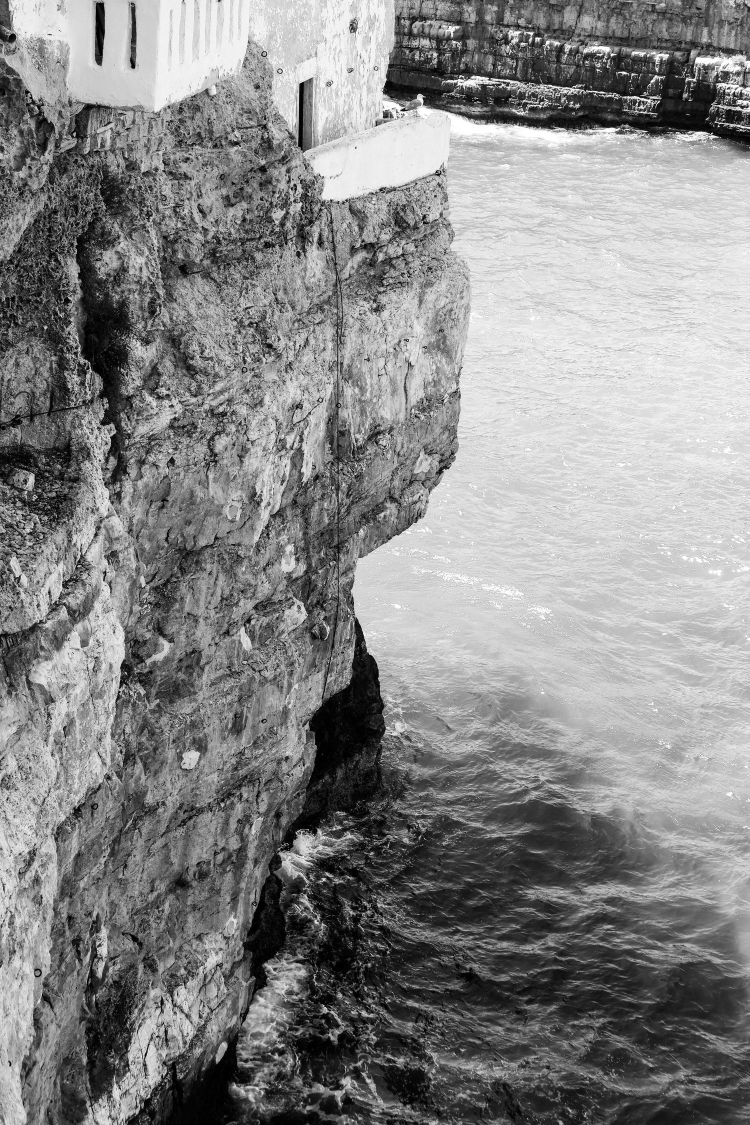 Dramatic black and white view of waves meeting limestone cliffs along the Mediterranean coastline.