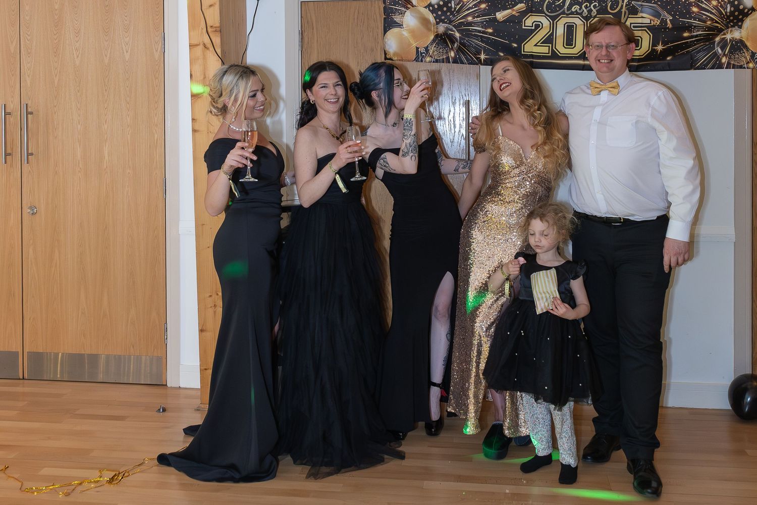 Group of elegantly dressed women in black and gold gowns celebrating New Year's Eve 2025 at a formal party.