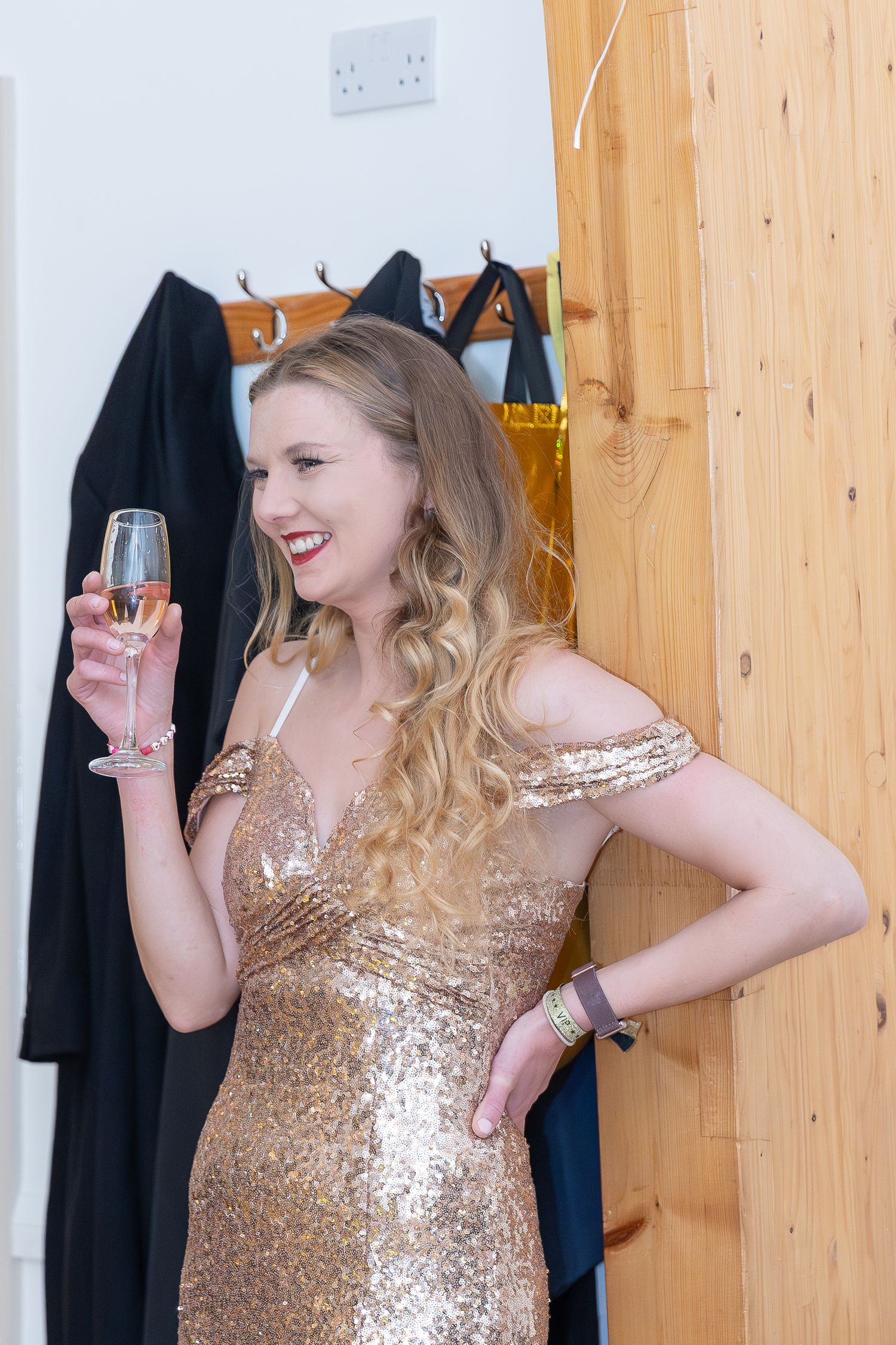 Woman in gold sequin dress holding champagne glass, smiling elegantly at a celebration.